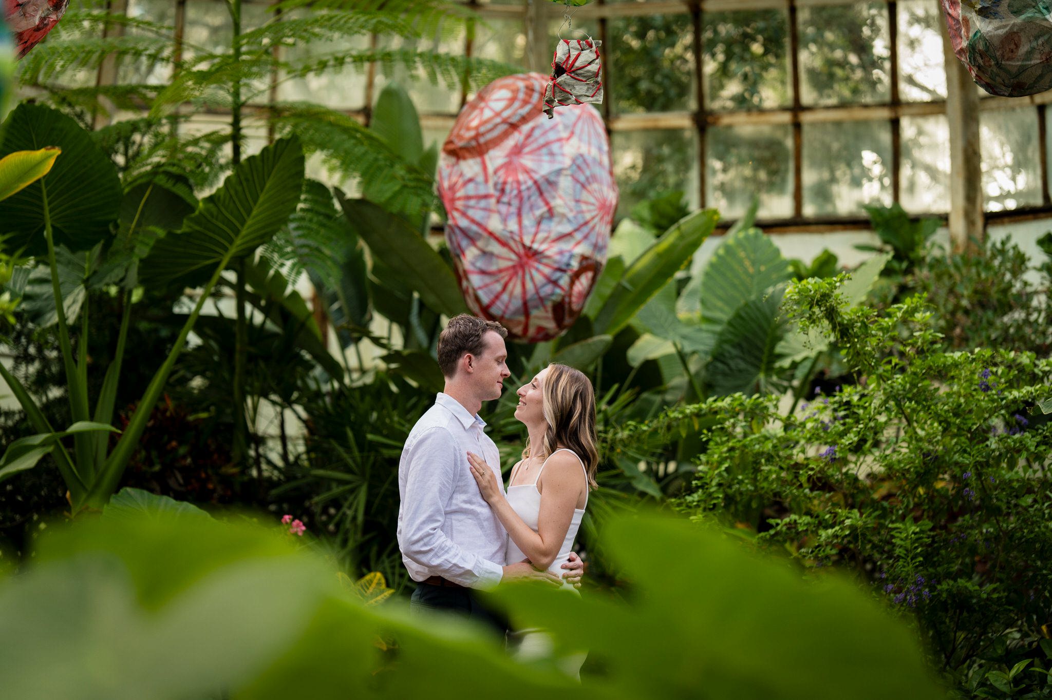 With a big leaf in the foreground, a couples poses during their engagement session at the Lincoln Park Conservatory in Chicago.  