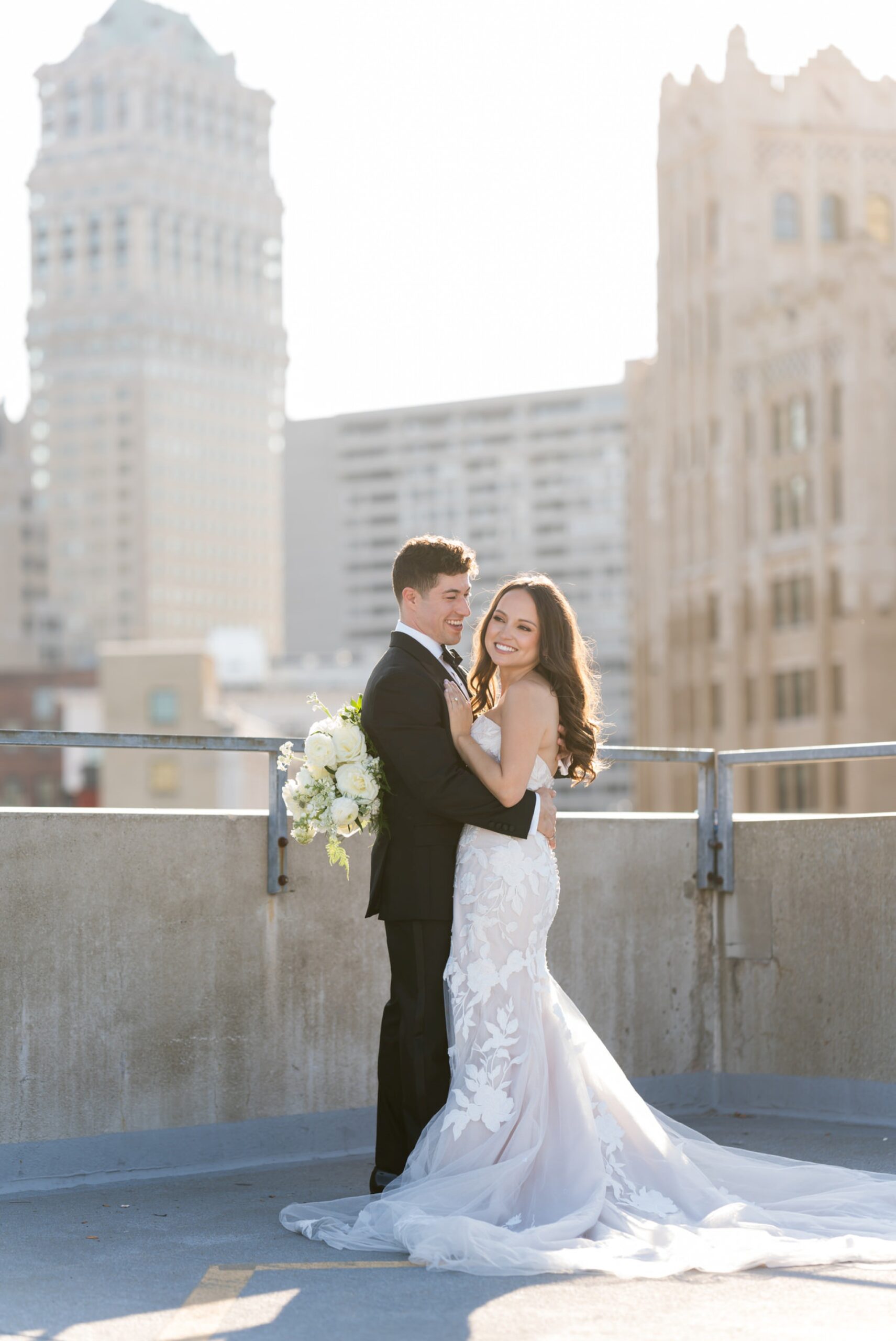 A bride and groom pose on top of a Detroit rooftop during golden hour.  