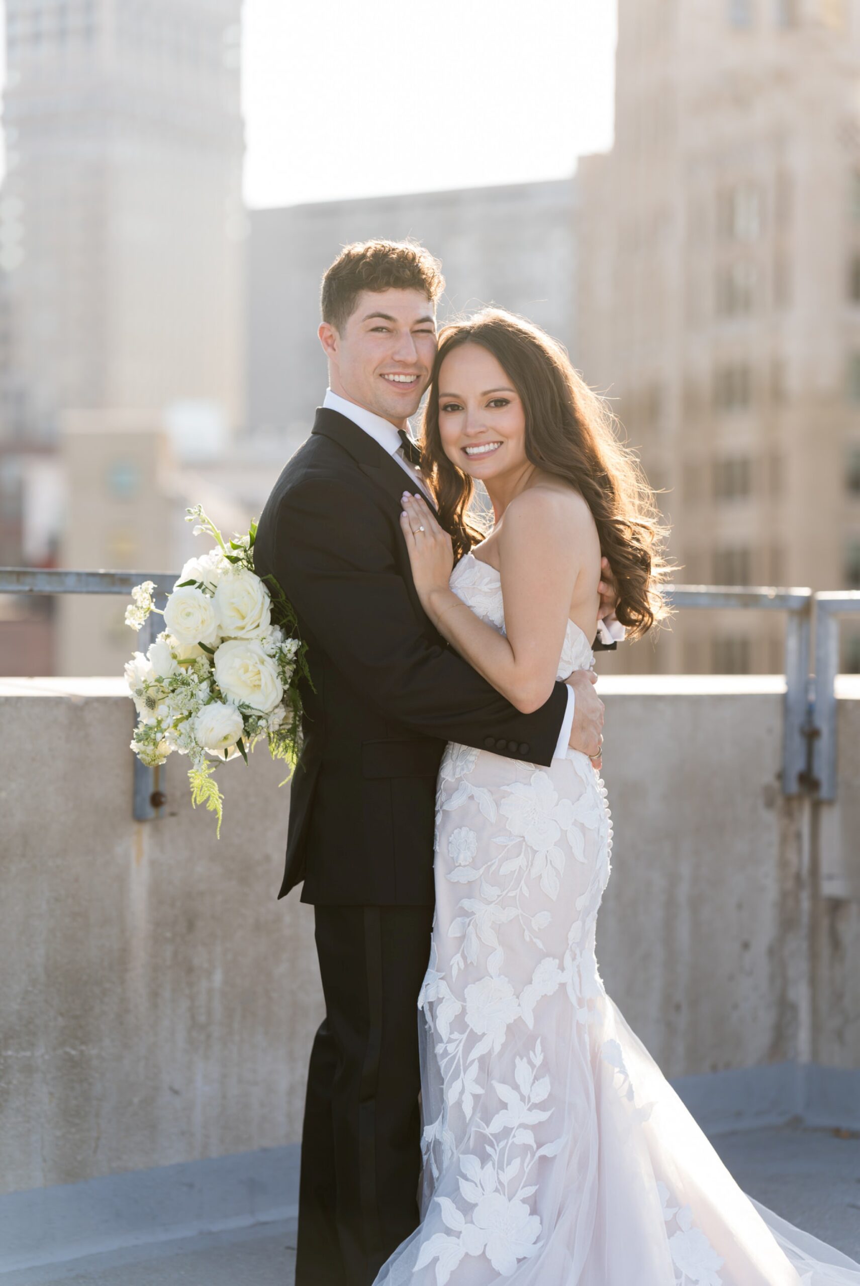 A bride and groom pose on top of a Detroit rooftop during golden hour.  