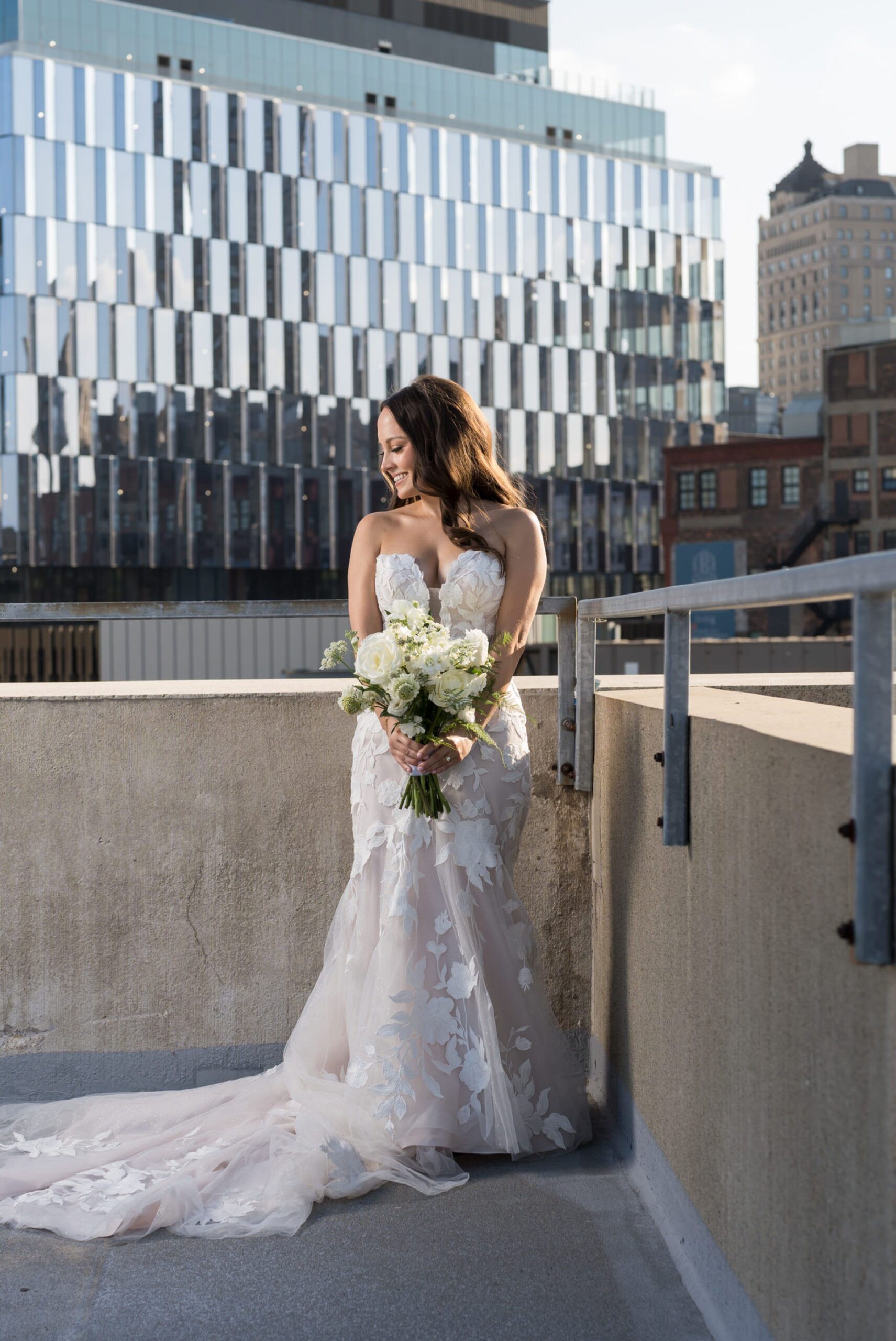 A bride poses with a Detroit skyscraper in the background on her wedding day.  