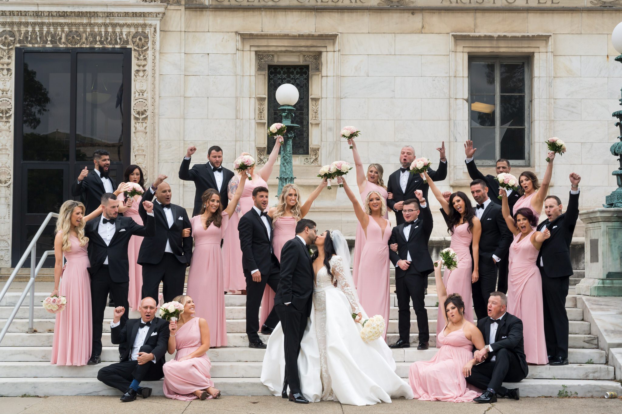 A bridal party, wearing pink and black, poses on the steps of the Detroit Public Library.