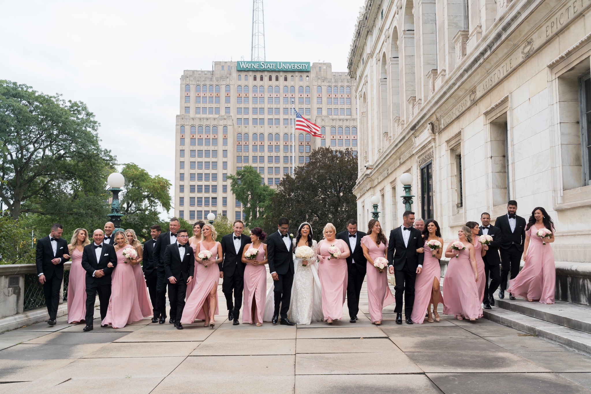 A bridal party, wearing pink and black, walks along the patio of the Detroit Public Library.