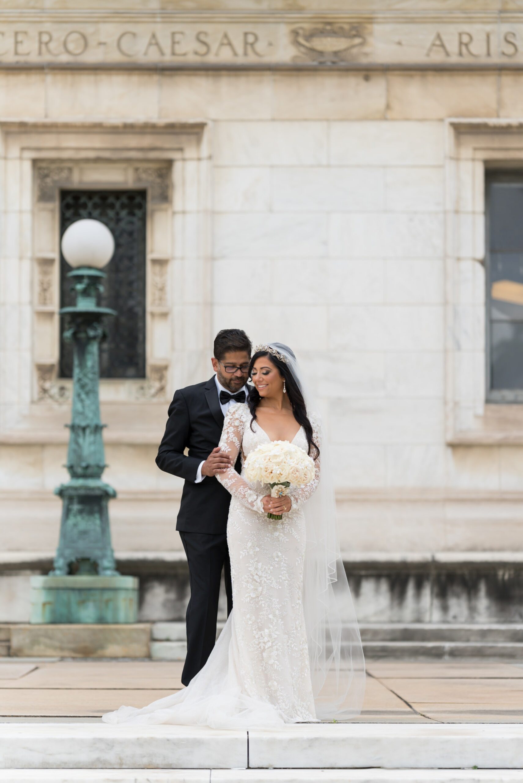 The bride and groom smile and pose on the steps of Detroit Public Library on Woodward on their wedding day. 