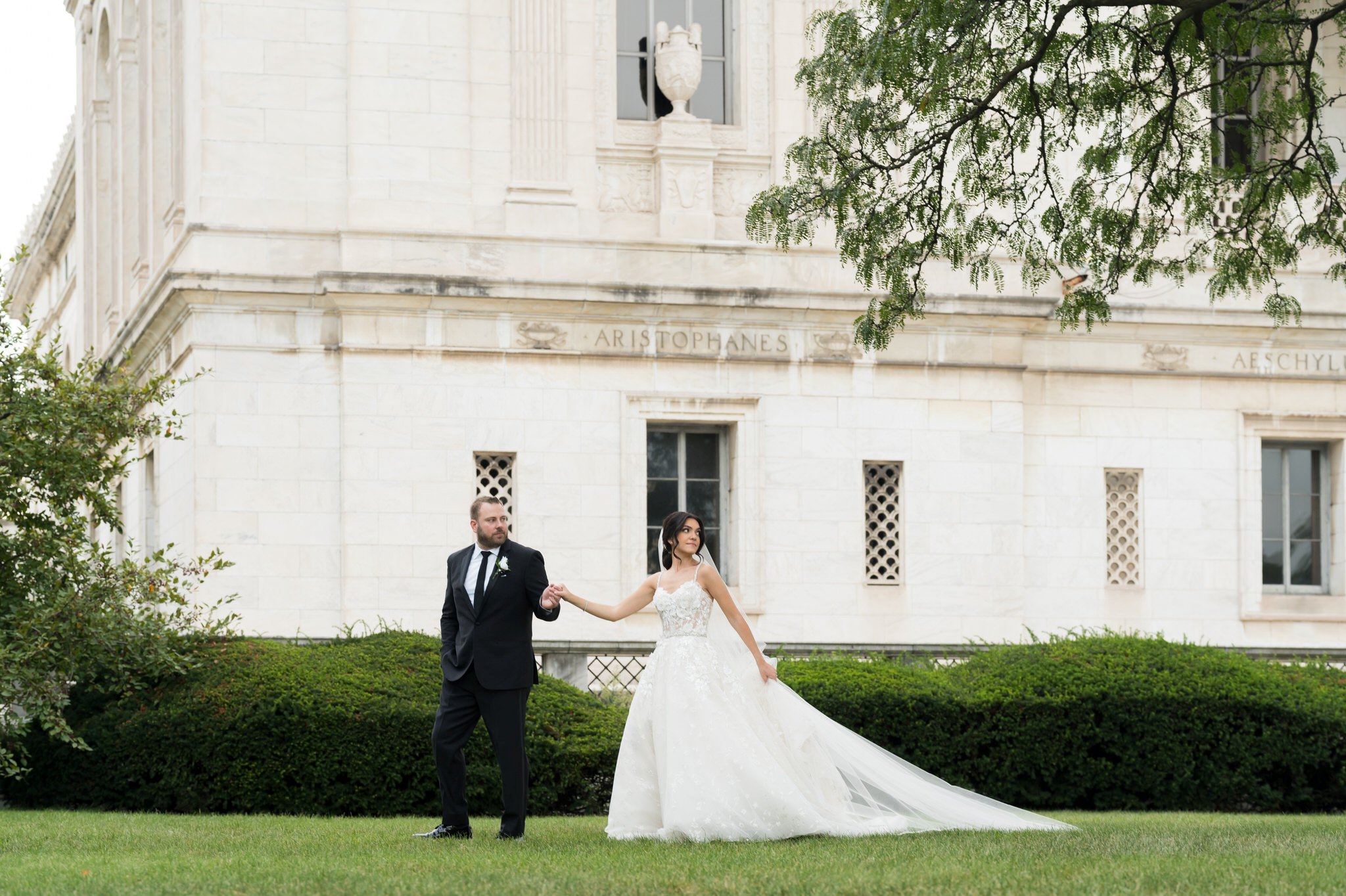 A bride and groom walk across the front lawn of the Detroit Public Library on Woodward.  