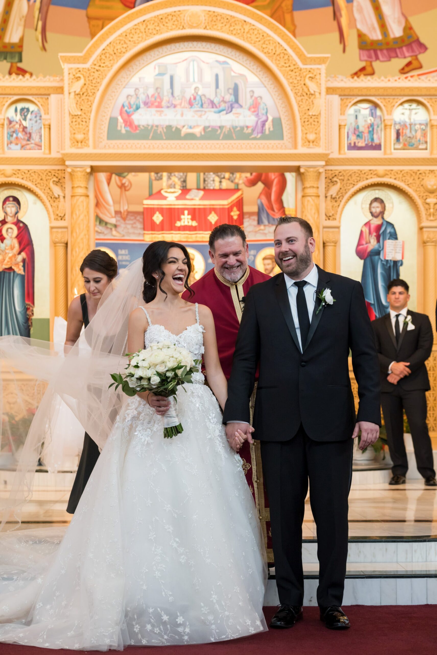 A bride and groom laugh at the altar during their Assumption Greek Orthodox wedding in St. Clair Shores, Michigan.
