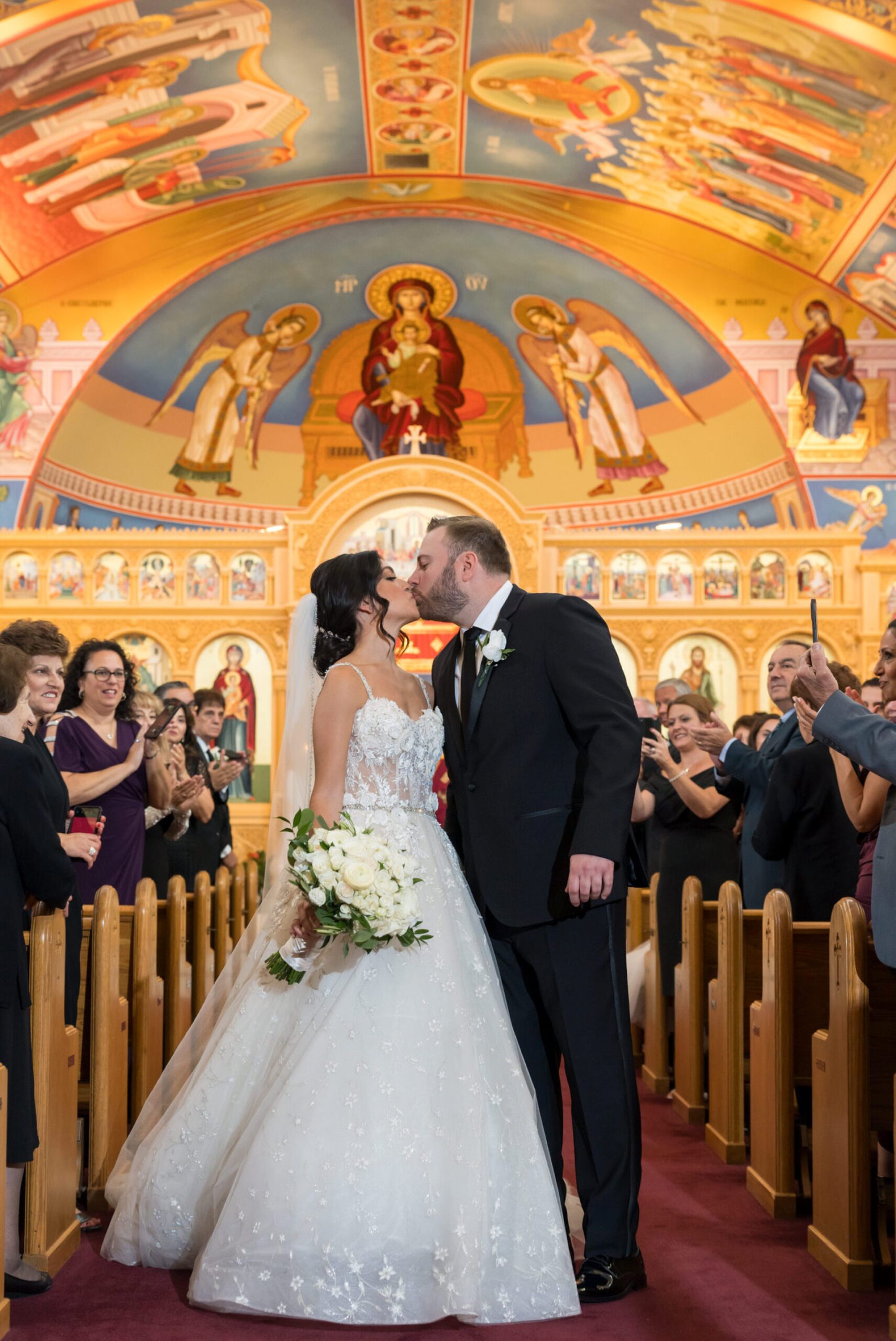 A bride and groom kiss down the center aisle during their Assumption Greek Orthodox wedding in St. Clair Shores, Michigan.