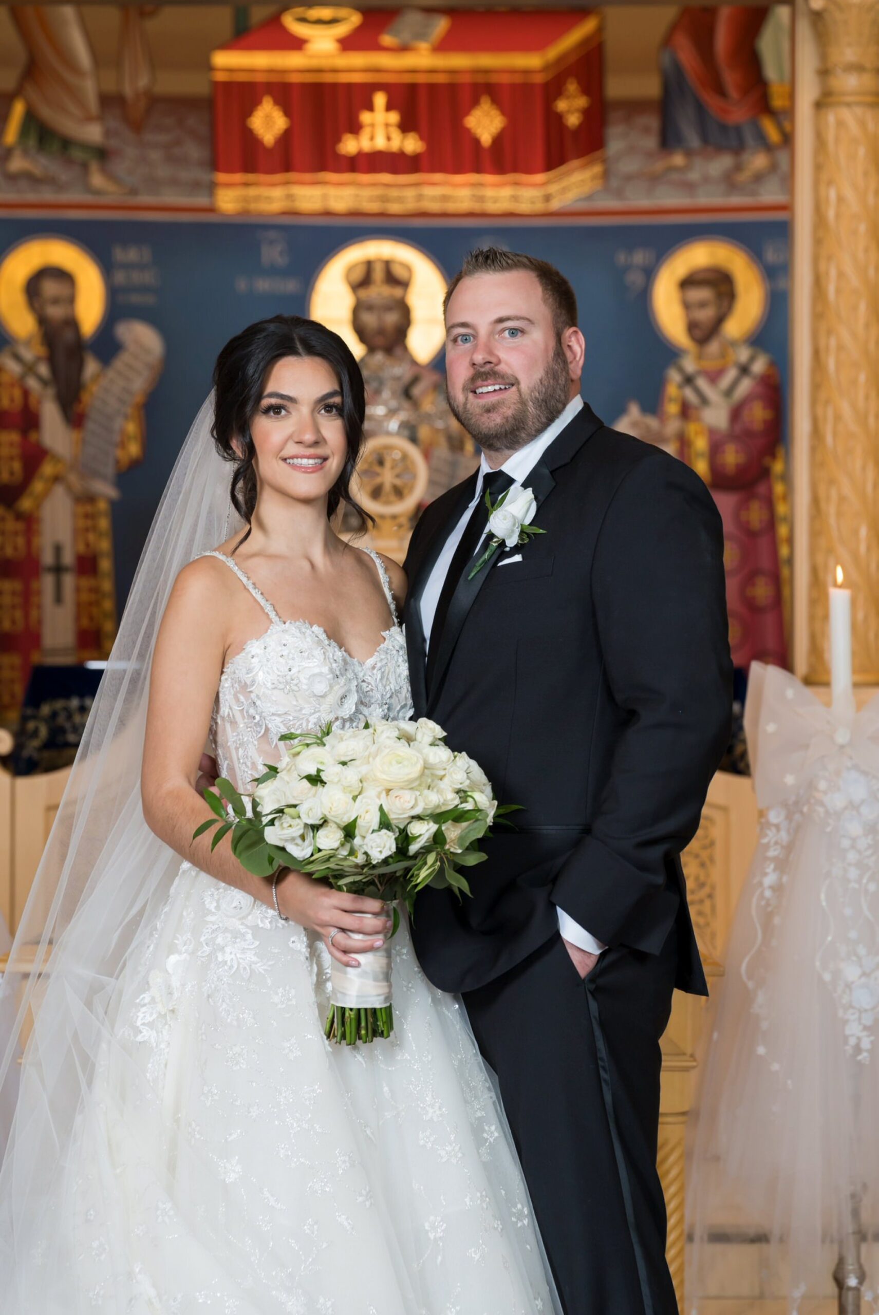 The bride and groom pose at the altar of their Assumption Greek Orthodox wedding for a formal portrait.  