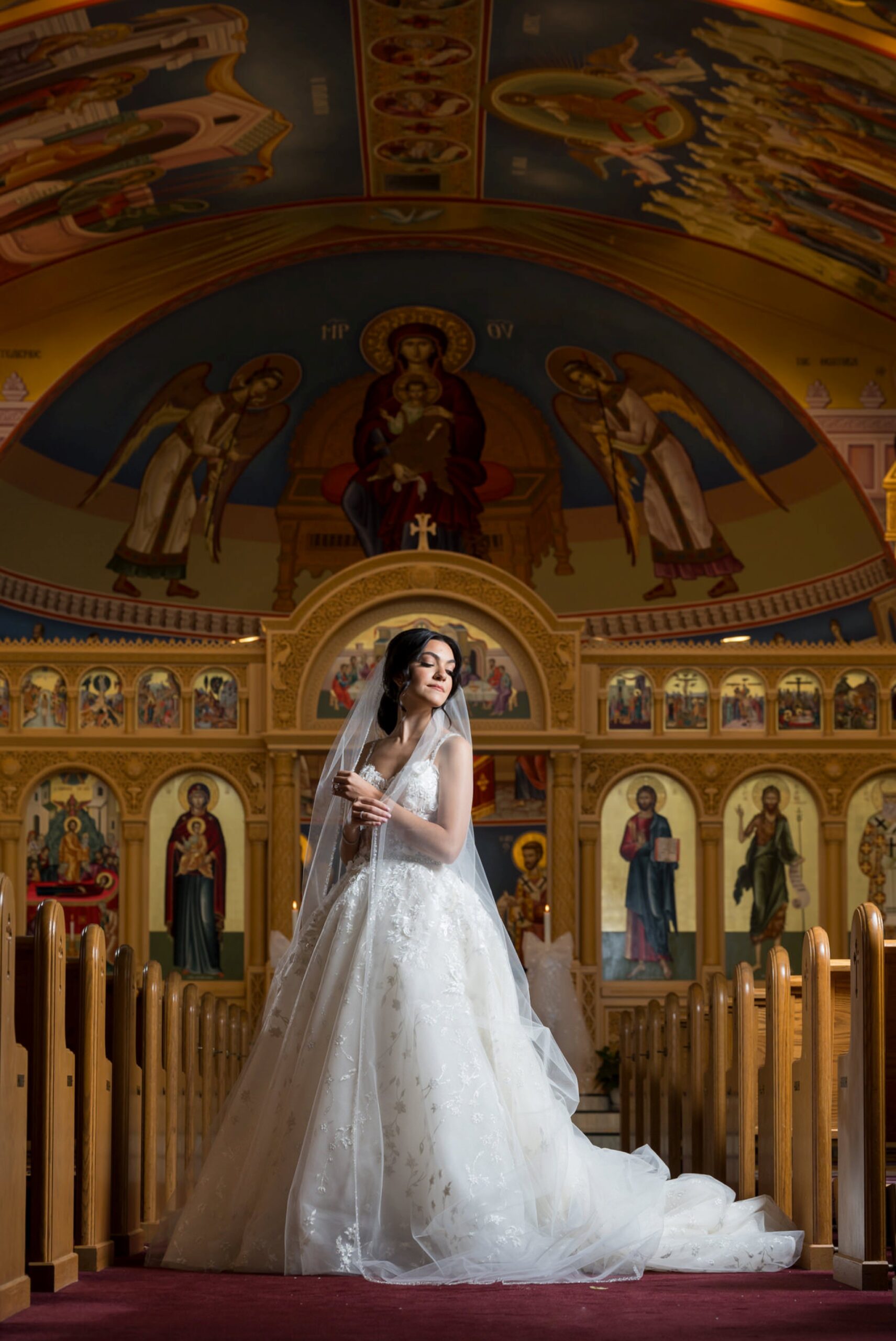 The bride poses in the center aisle of an Assumption Greek Orthodox wedding.