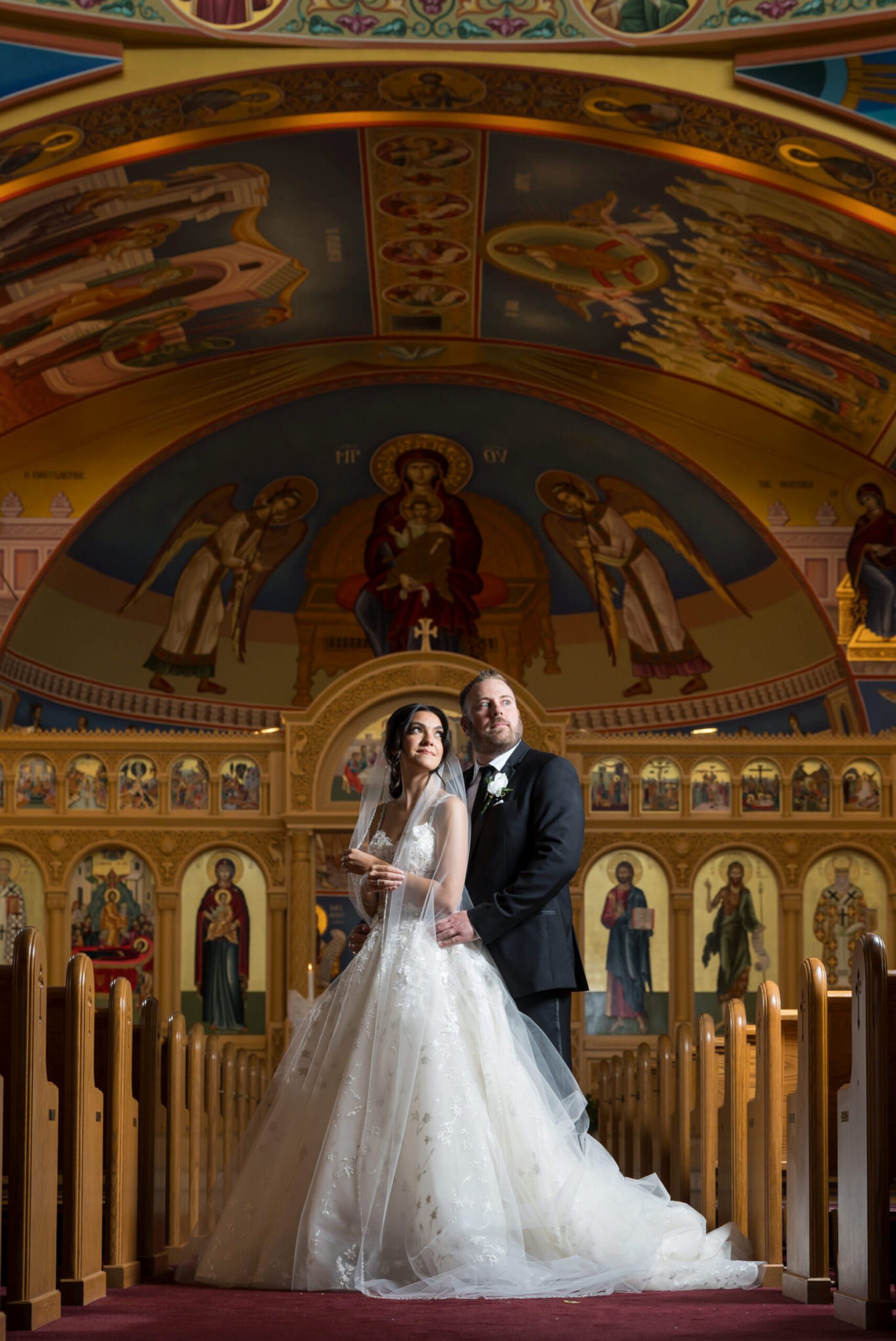 The bride and groom pose in the center aisle of an Assumption Greek Orthodox wedding.
