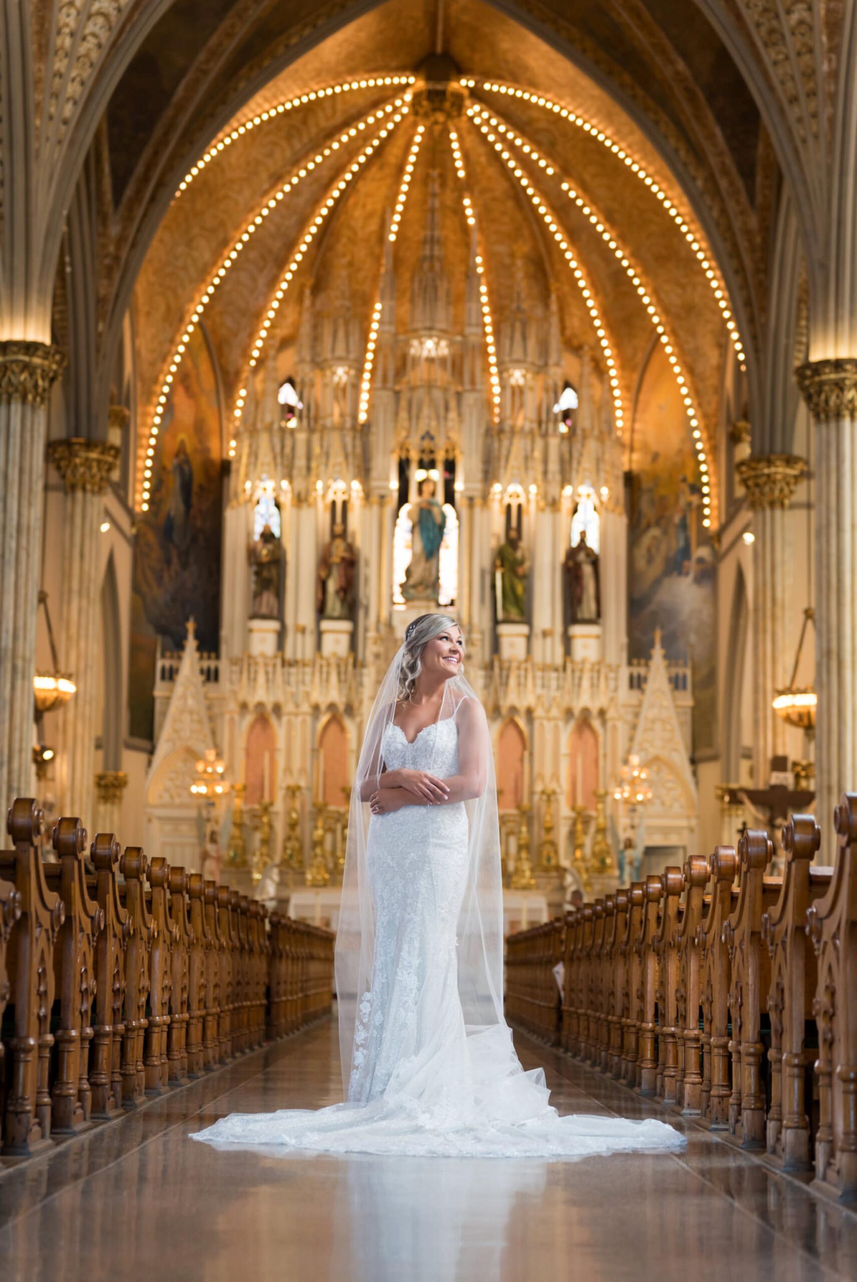 A bride poses while holding her veil in the center aisle of Detroit's Sweetest Heart of Mary Catholic Church.  
