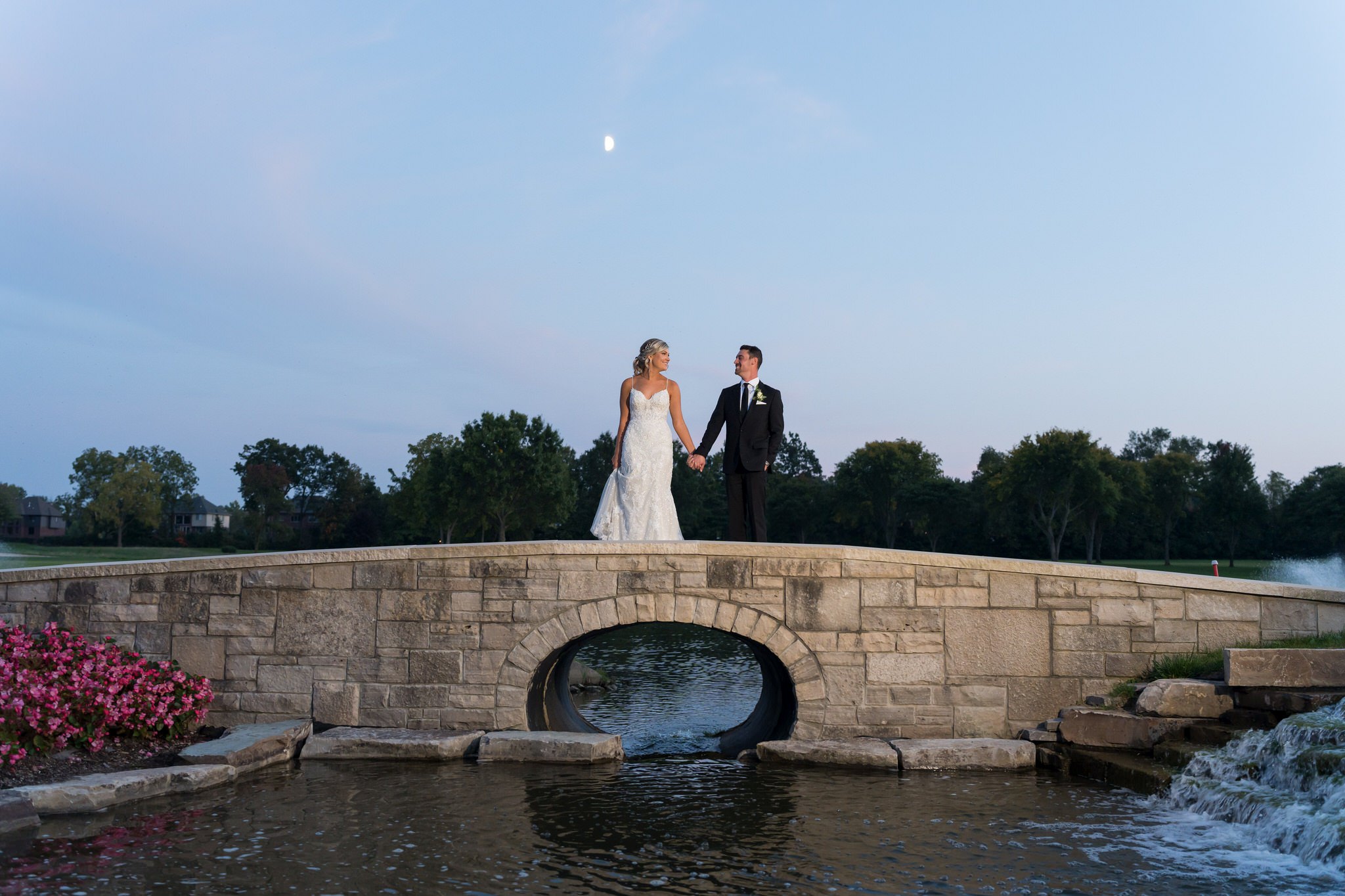 A bride and groom hold hands on the stone bridge at their Walnut Creek Golf Club wedding in South Lyon, MI.  