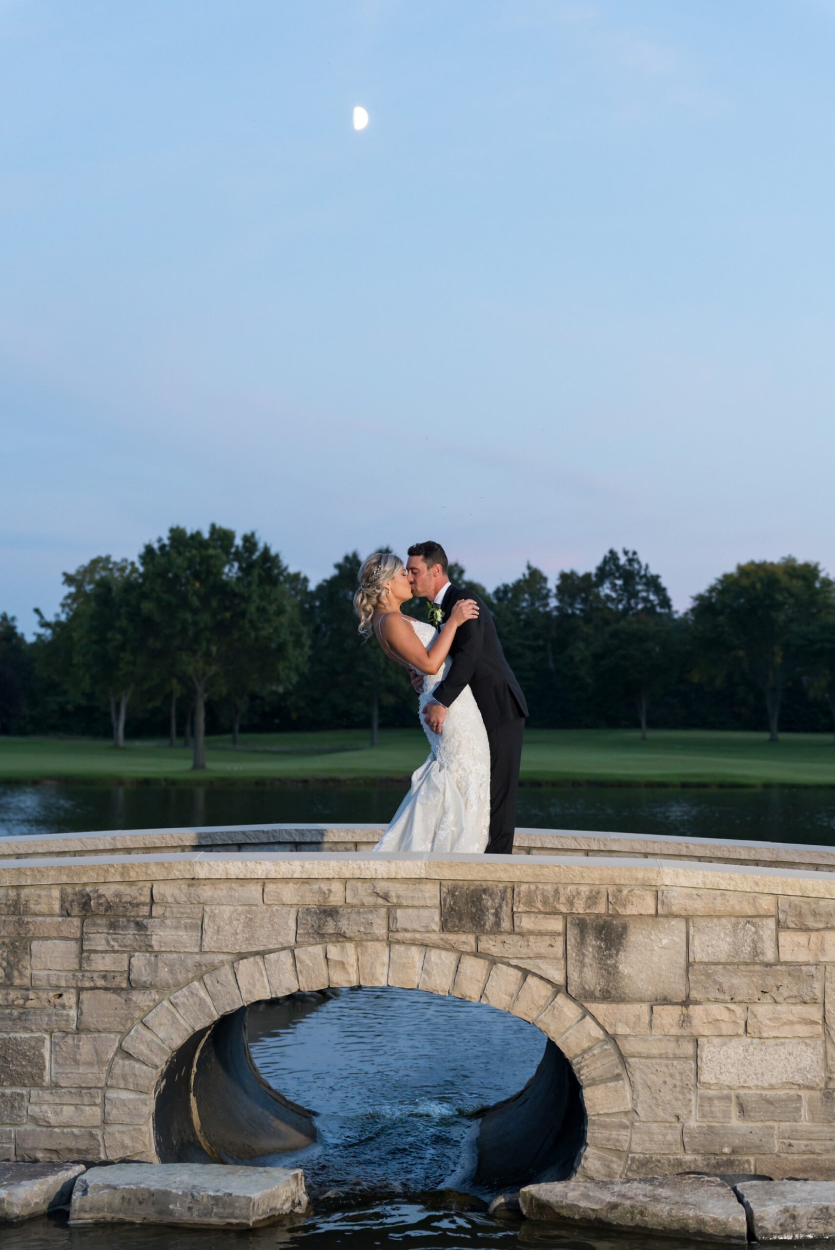 A bride and groom kiss on a stone bridge at their Walnut Creek Golf Club wedding in South Lyon, MI.  