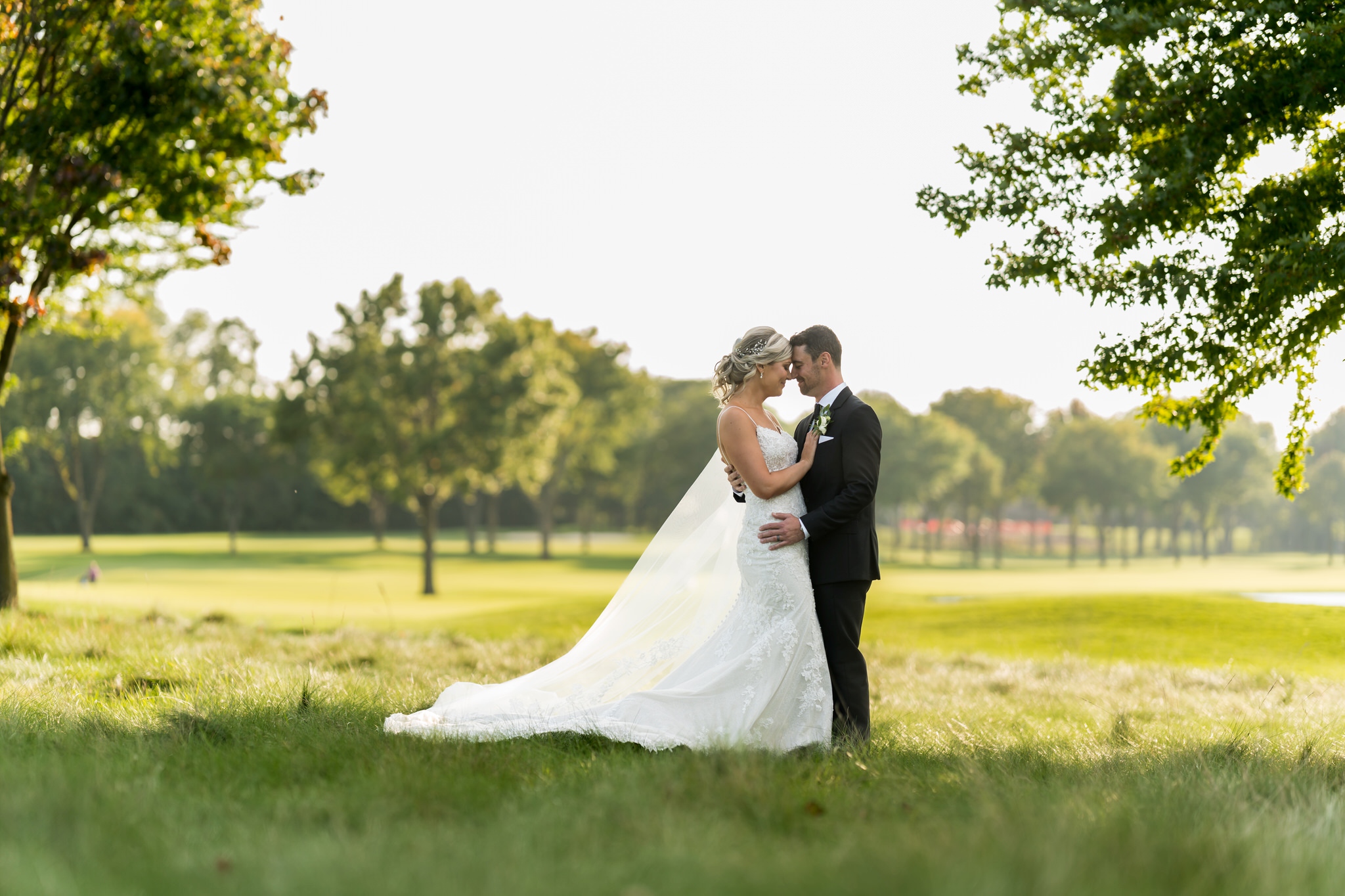 A bride and groom hug standing in tall grass at their Walnut Creek Golf Club wedding in South Lyon, MI.  