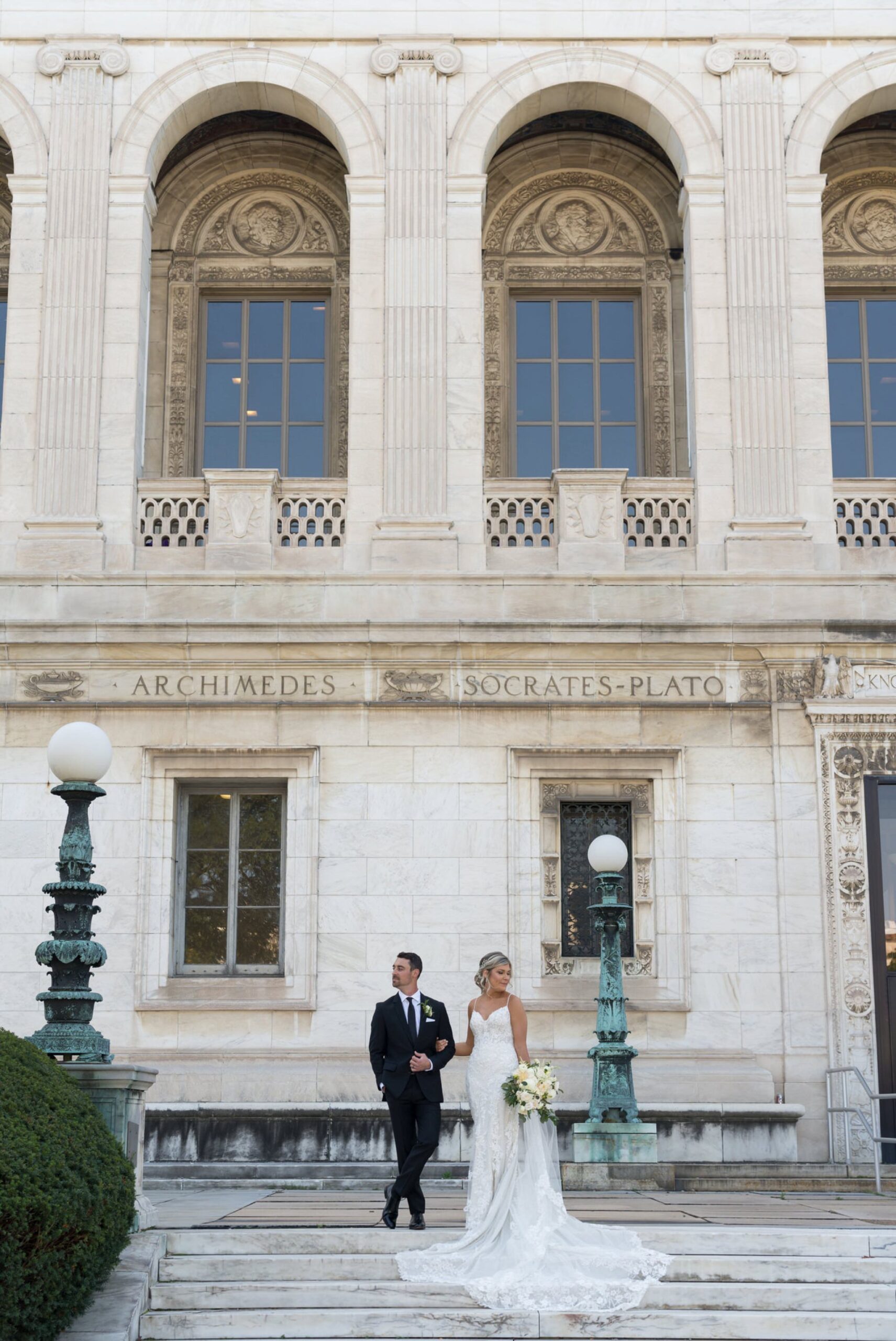 A bride holds the arm of the groom on the steps of the Detroit Public Library.  a