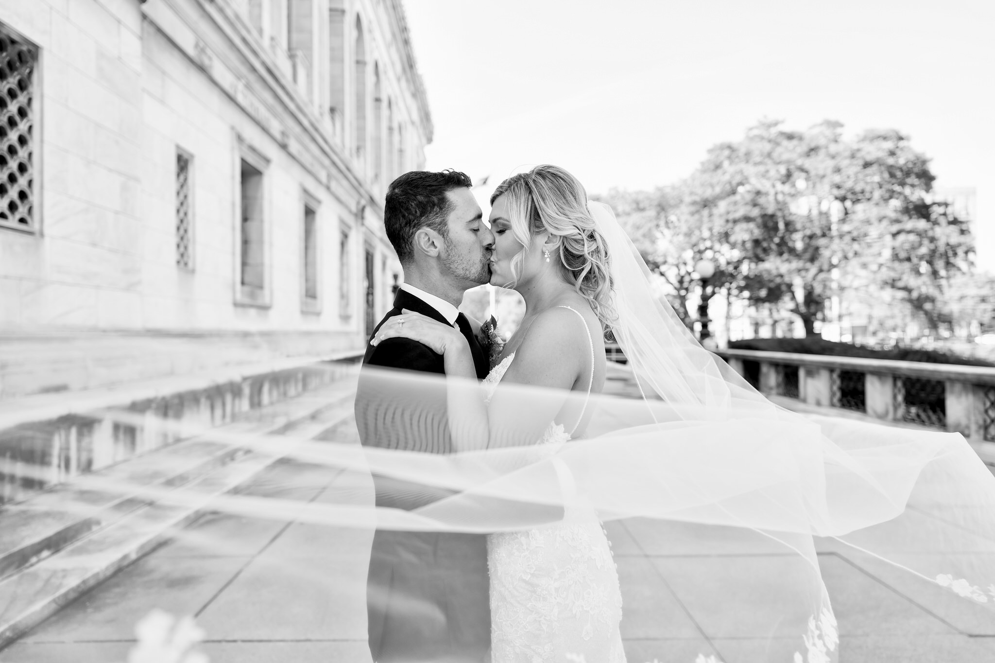 A bride and groom embrace and kiss on the front porch of the Detroit Public Library on their wedding day.  
