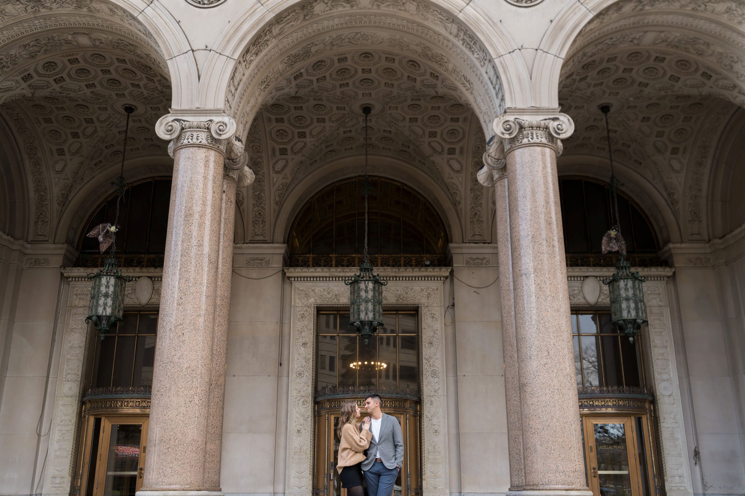 A couple poses outside of Cadillac Place Apartments in Detroit during their engagement session.  
