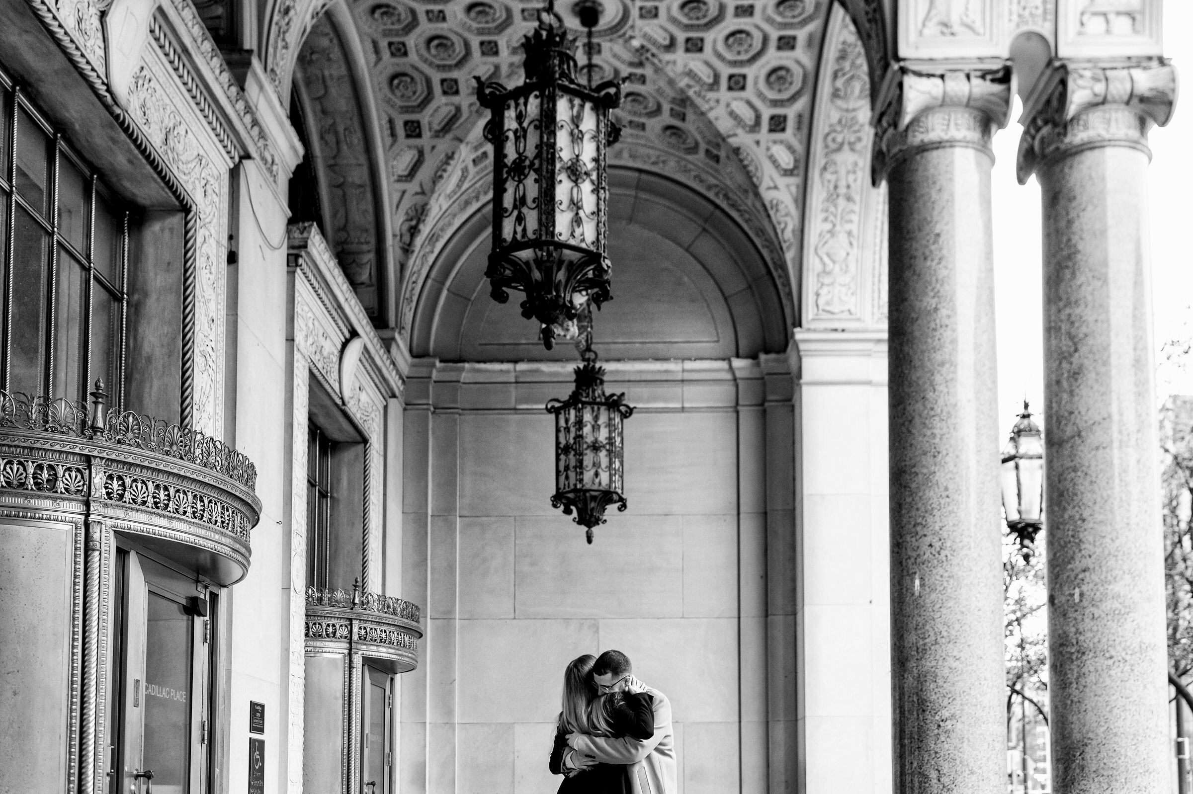 A couple shares a moment and hugs under a chandelier after a Cadillac Place proposal in Detroit.  