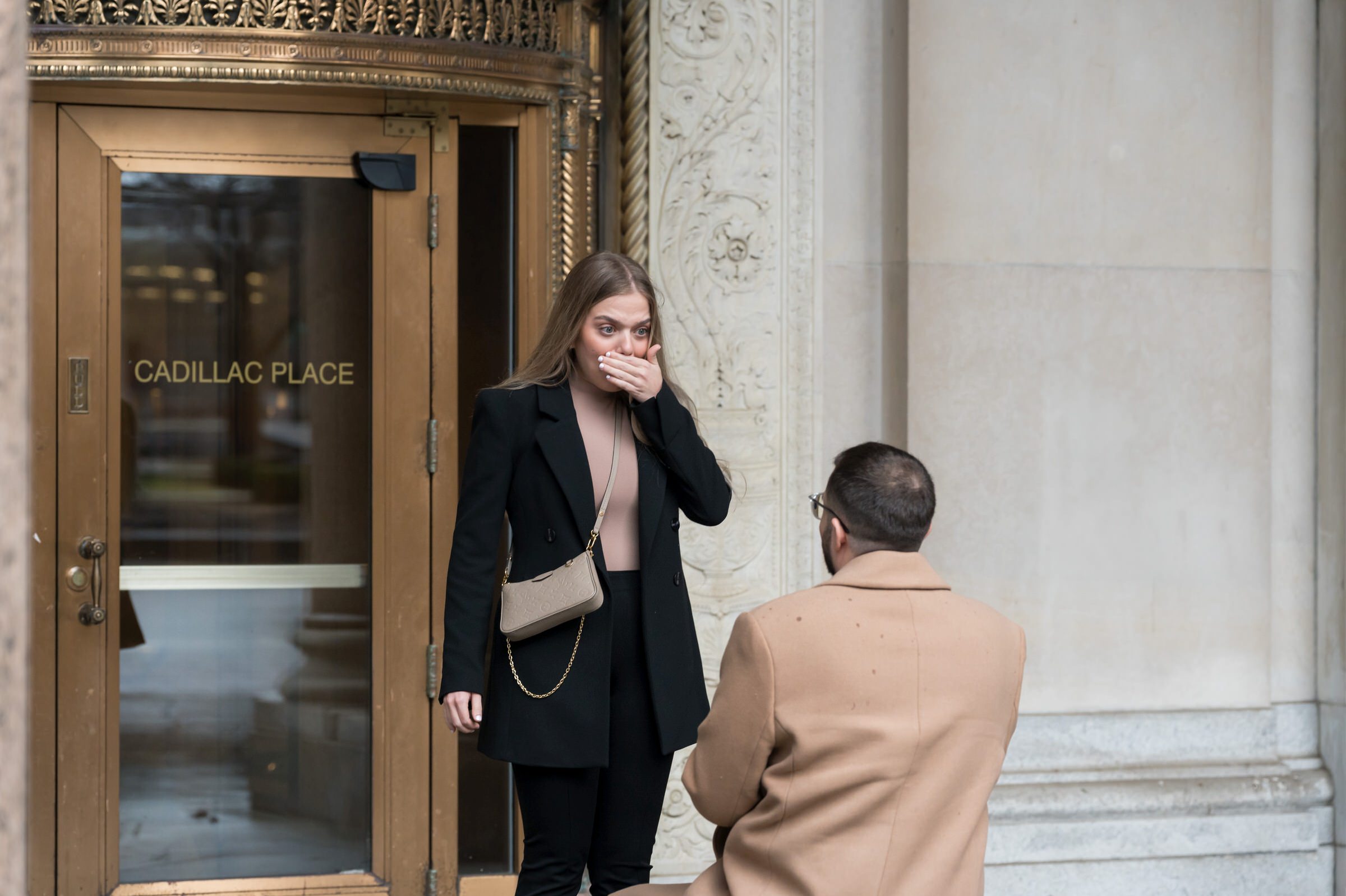 A fiancee covers her mouth in disbelief during her Cadillac Place proposal. 
