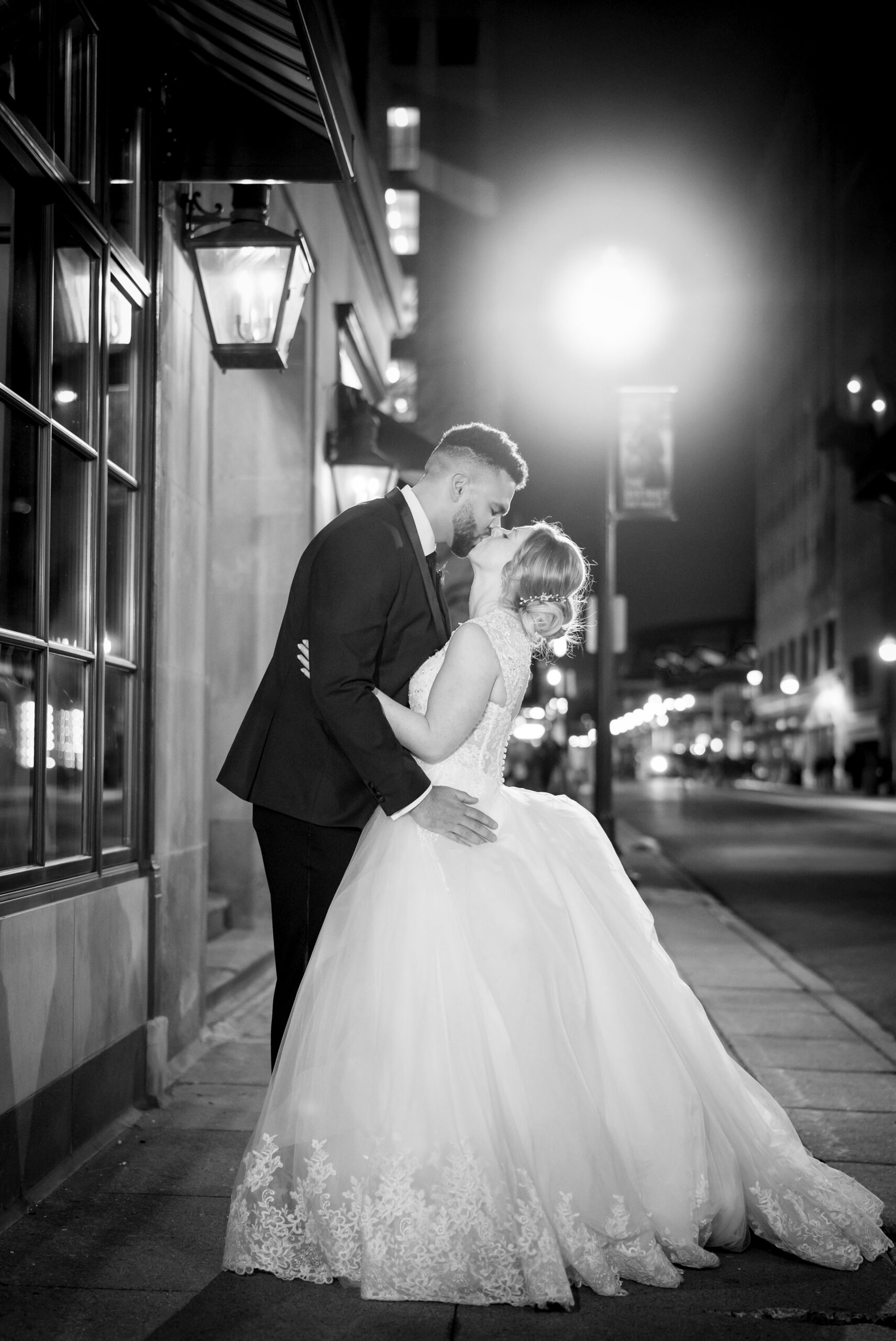 A couple, standing under a street light, kisses outside of their Detroit Colony Club wedding reception.  