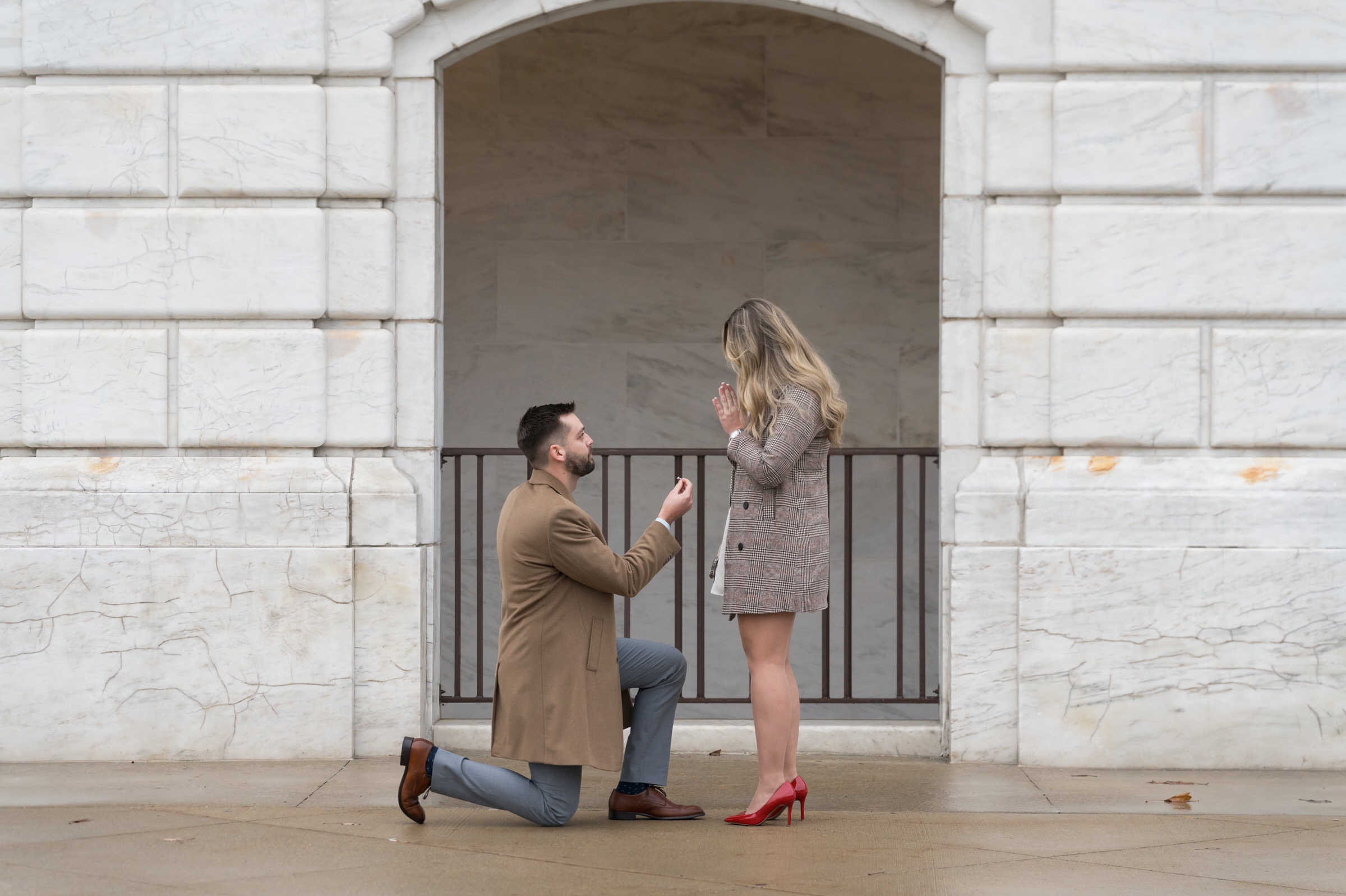 A man takes a knee, reaches into his coat pocket, offers his girlfriend and engagement ring at a Detroit Institute of Arts proposal.