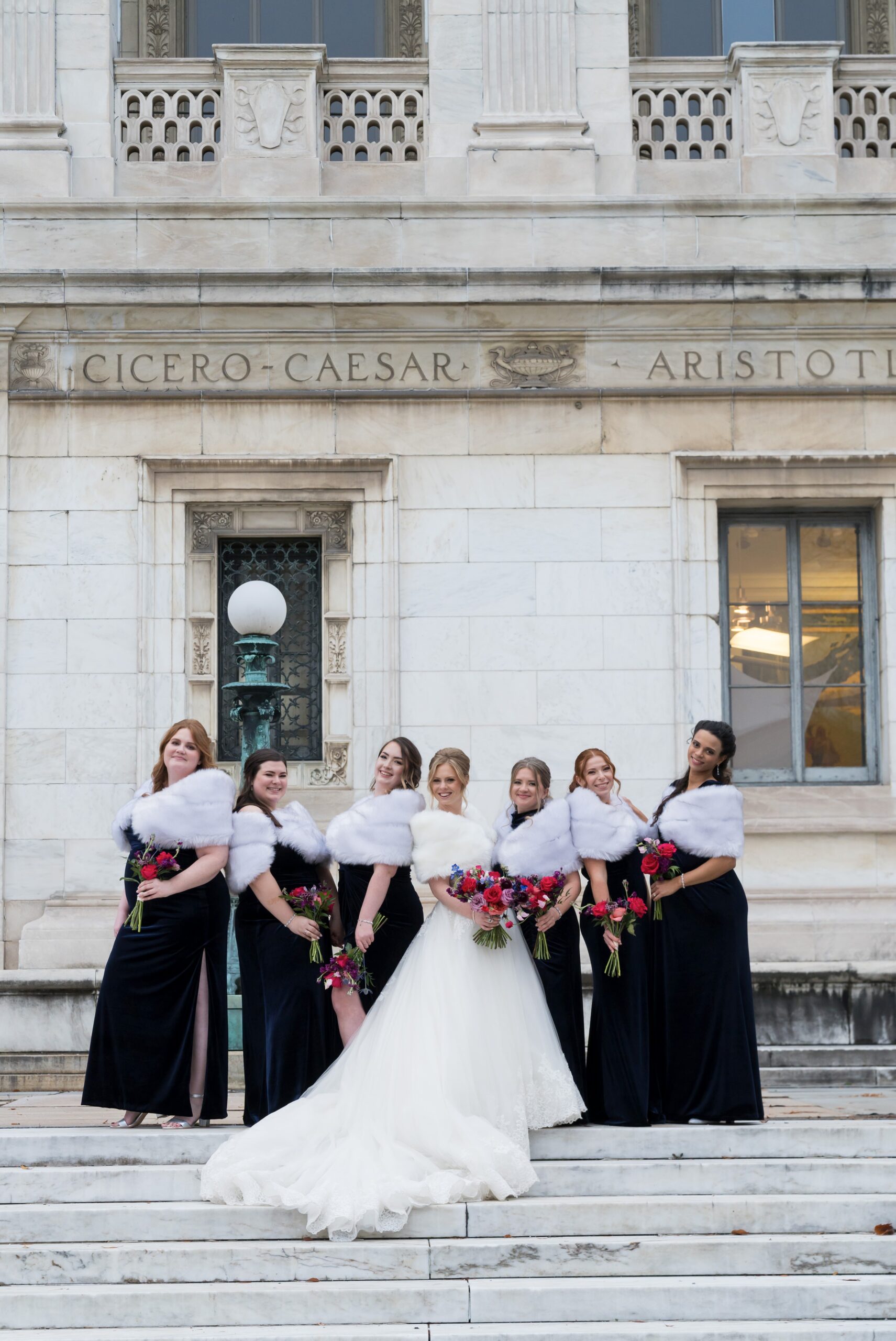 Bridesmaids, wearing shawls, pose for a photo on the steps of the Detroit Public Library.