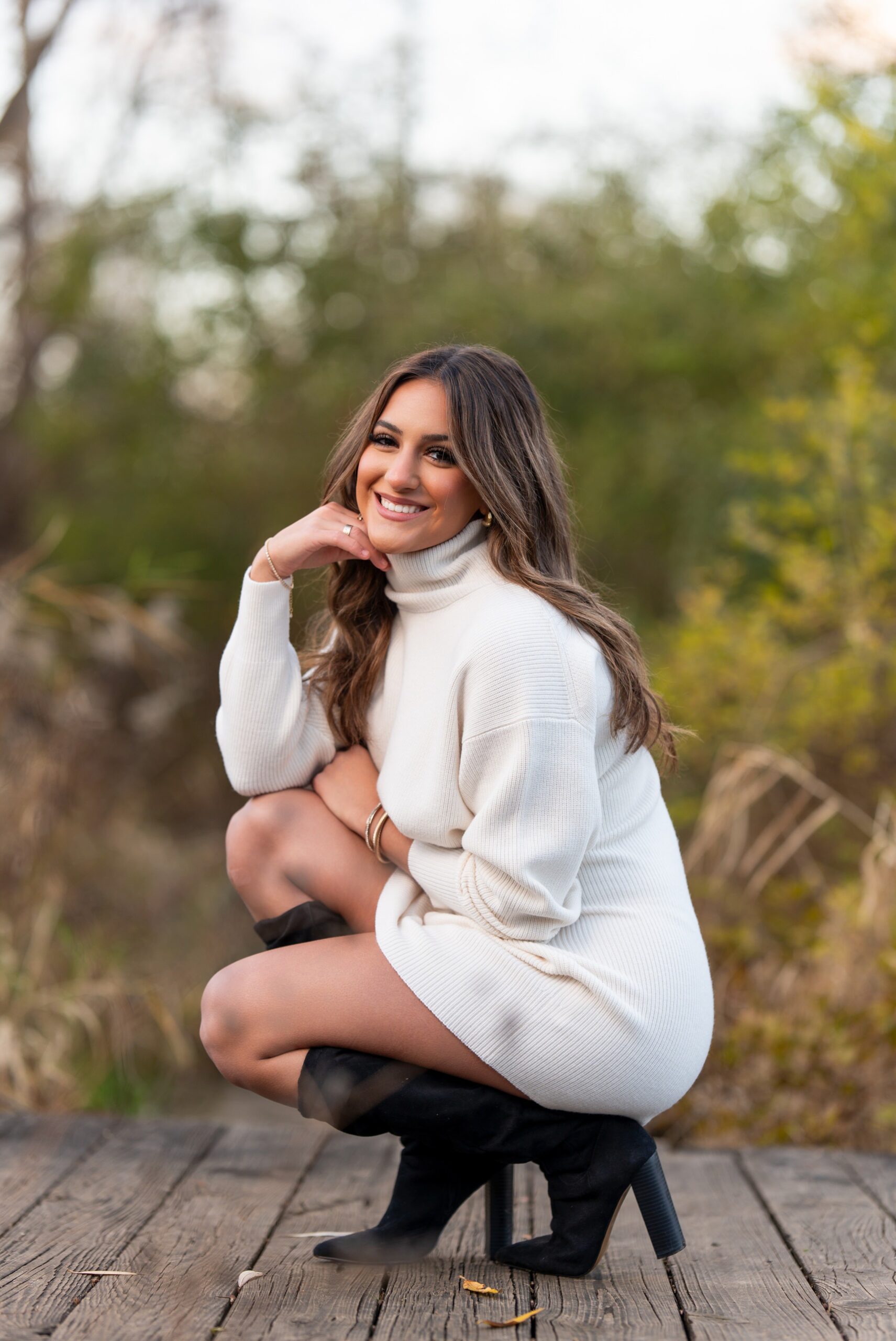 Wearing a cream colored sweater and black knee-high boots, a high school senior poses for her senior photos at Van Hoosen. 