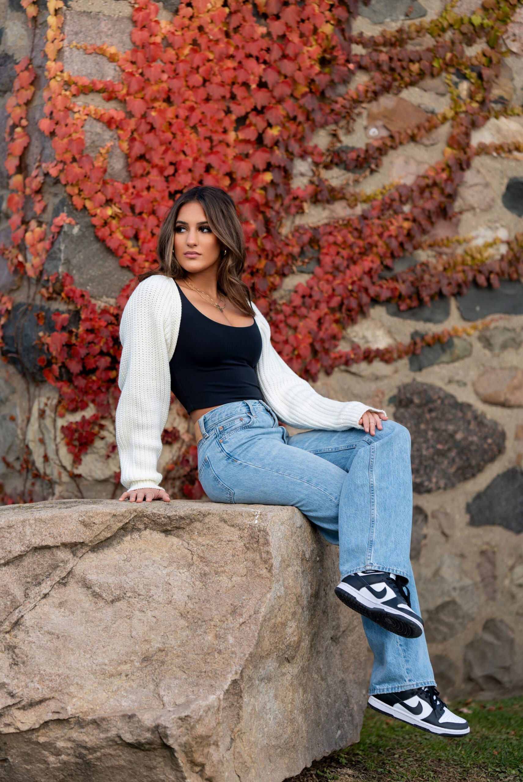 Sitting on a rock with a red leafed vine behind her, a high schooler poses for her senior photos at Van Hoosen.