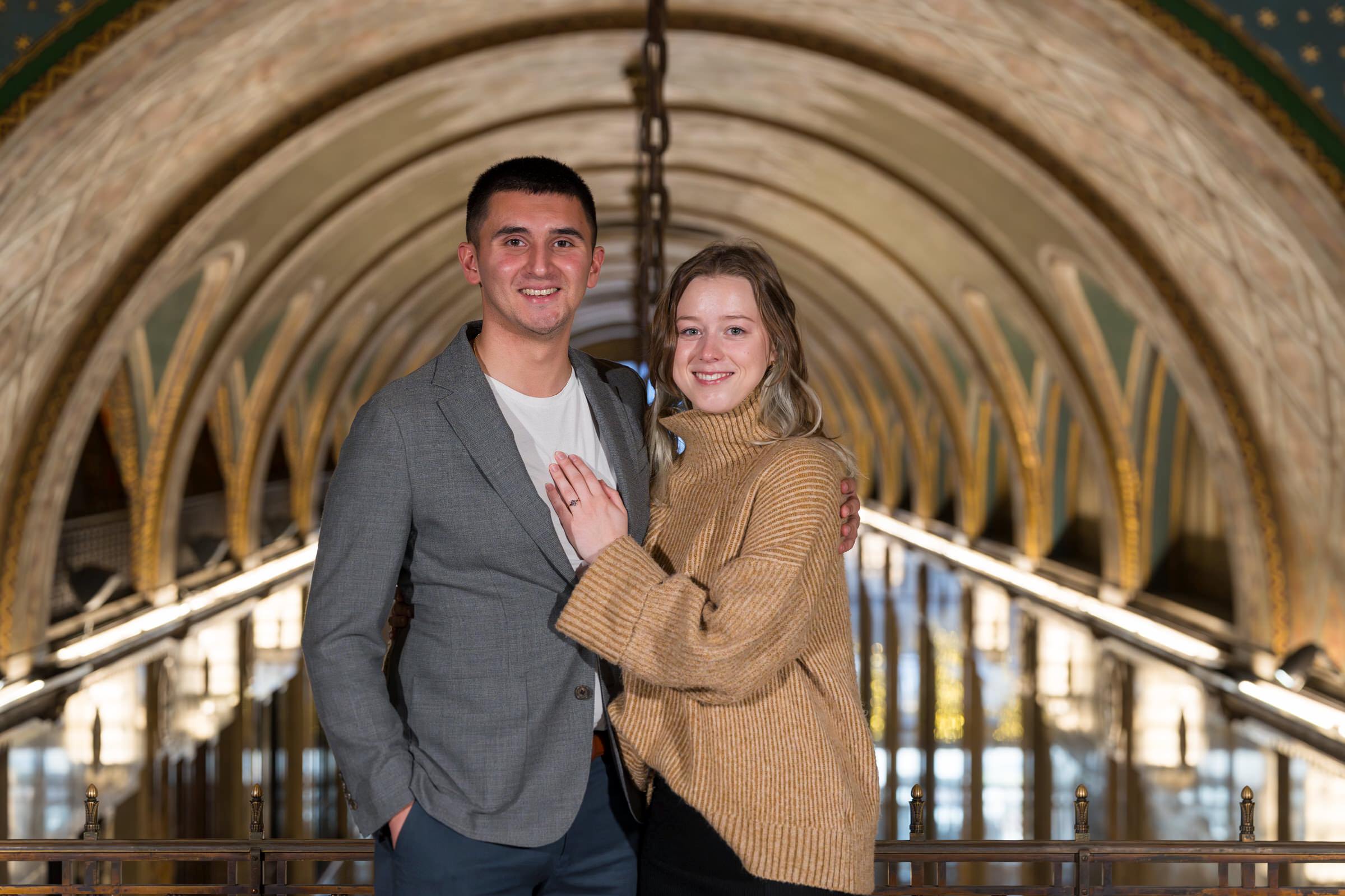 A couple poses, showing off a new engagement ring, after their Fisher Building proposal in Detroit, Michigan.  