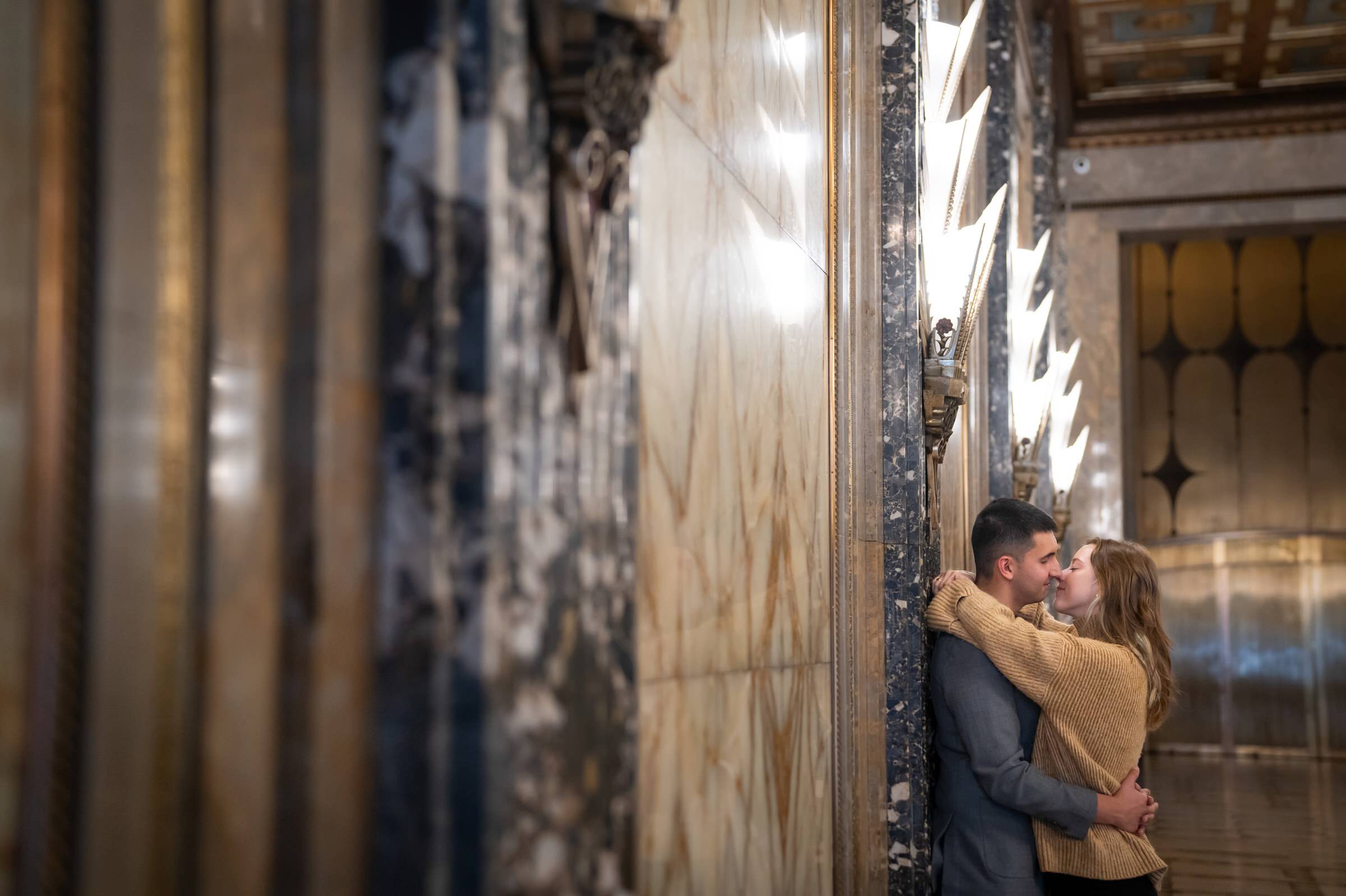 A couple almost kisses under art deco lights after their Fisher Building proposal.  