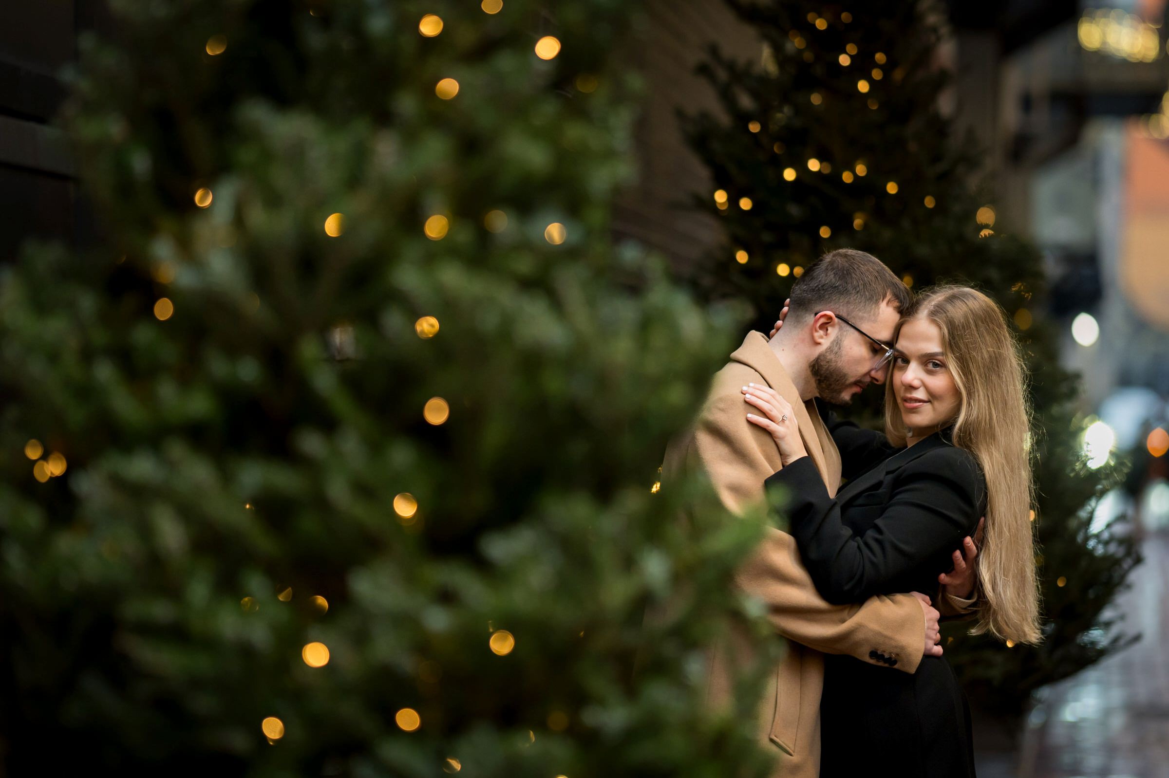 A couple embraces in between Christmas trees located in Parker's Alley during their engagement session.  