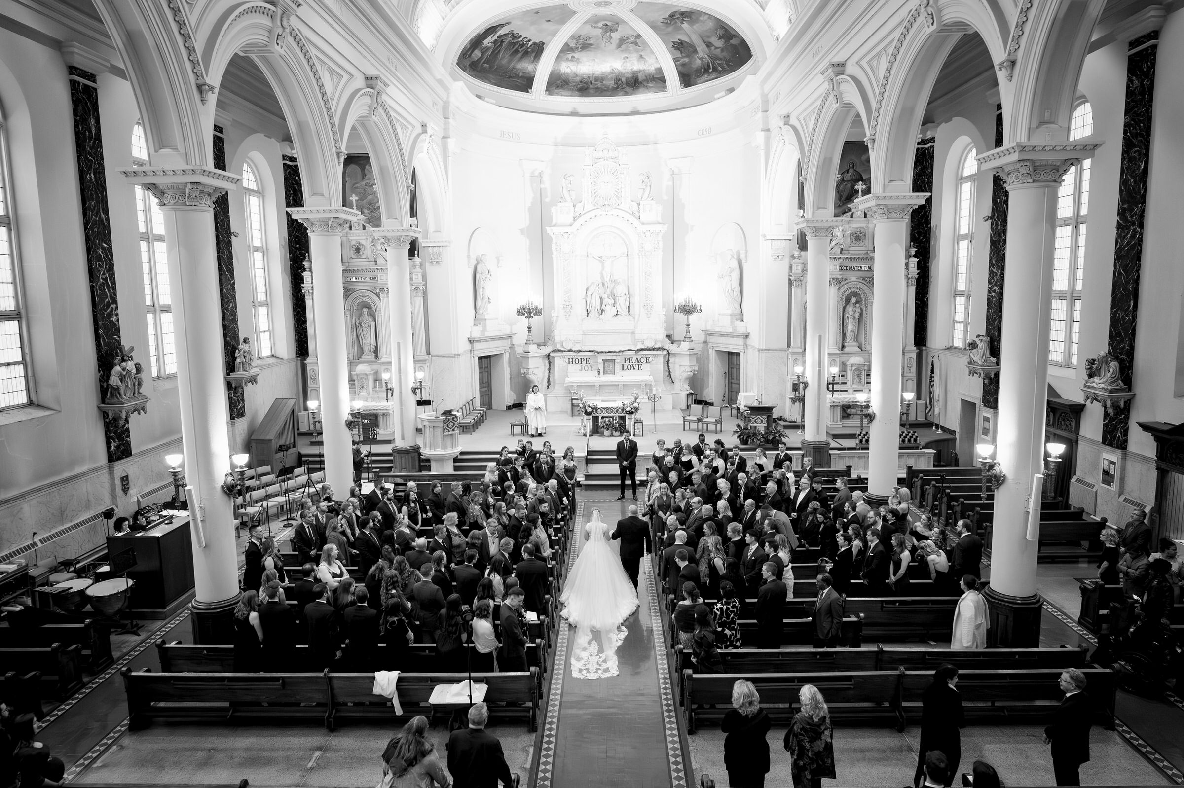 Taken from the balcony, a bride and her father walk down the aisle at Sts Peter and Paul Jesuit Church.  