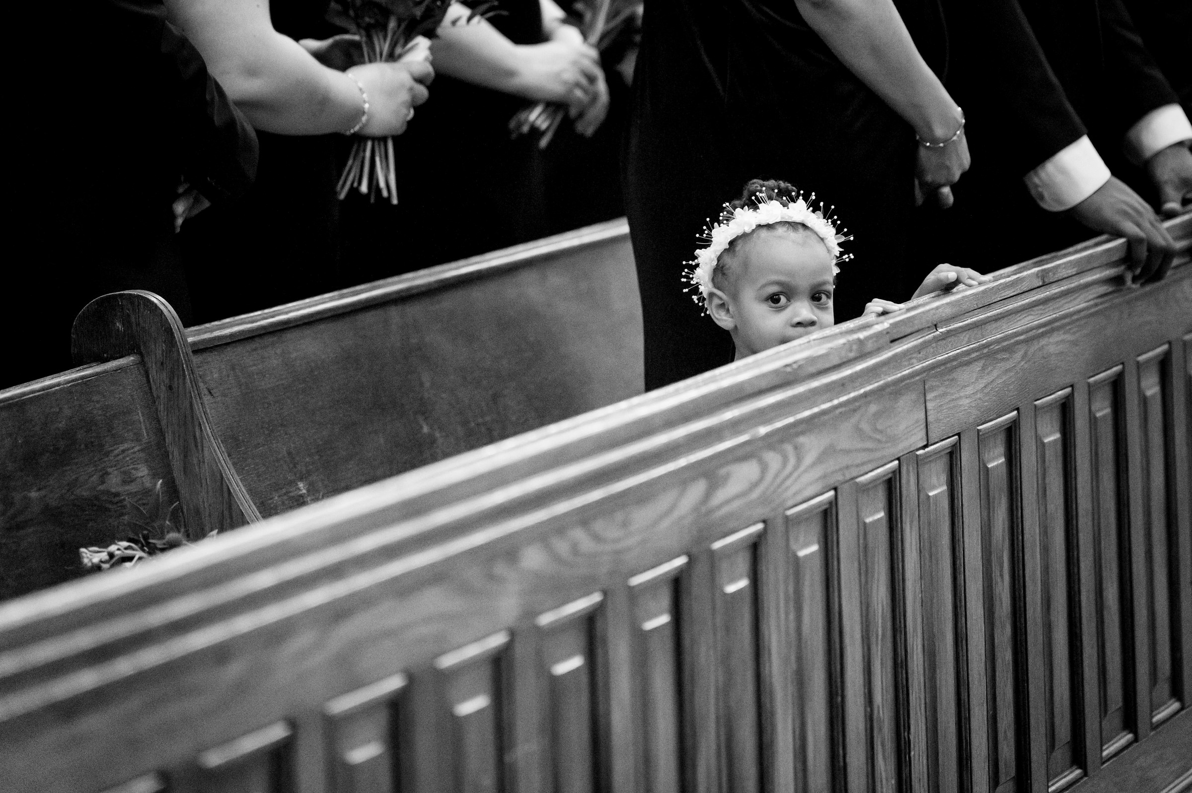 A little girl looks over the pew during a wedding ceremony.  