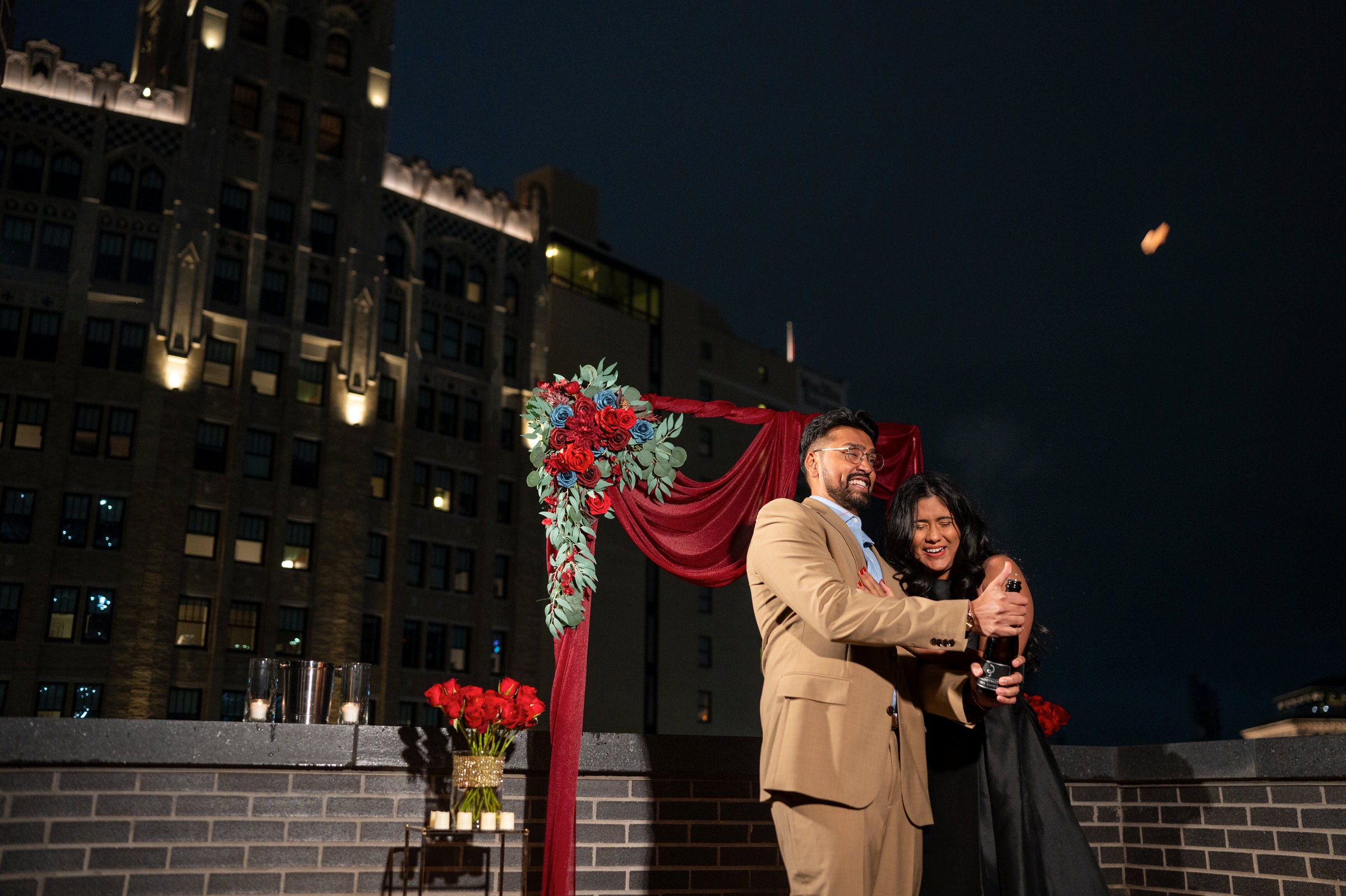 A couple pops a bottle of champagne on a rooftop after their Shinola Hotel proposal.