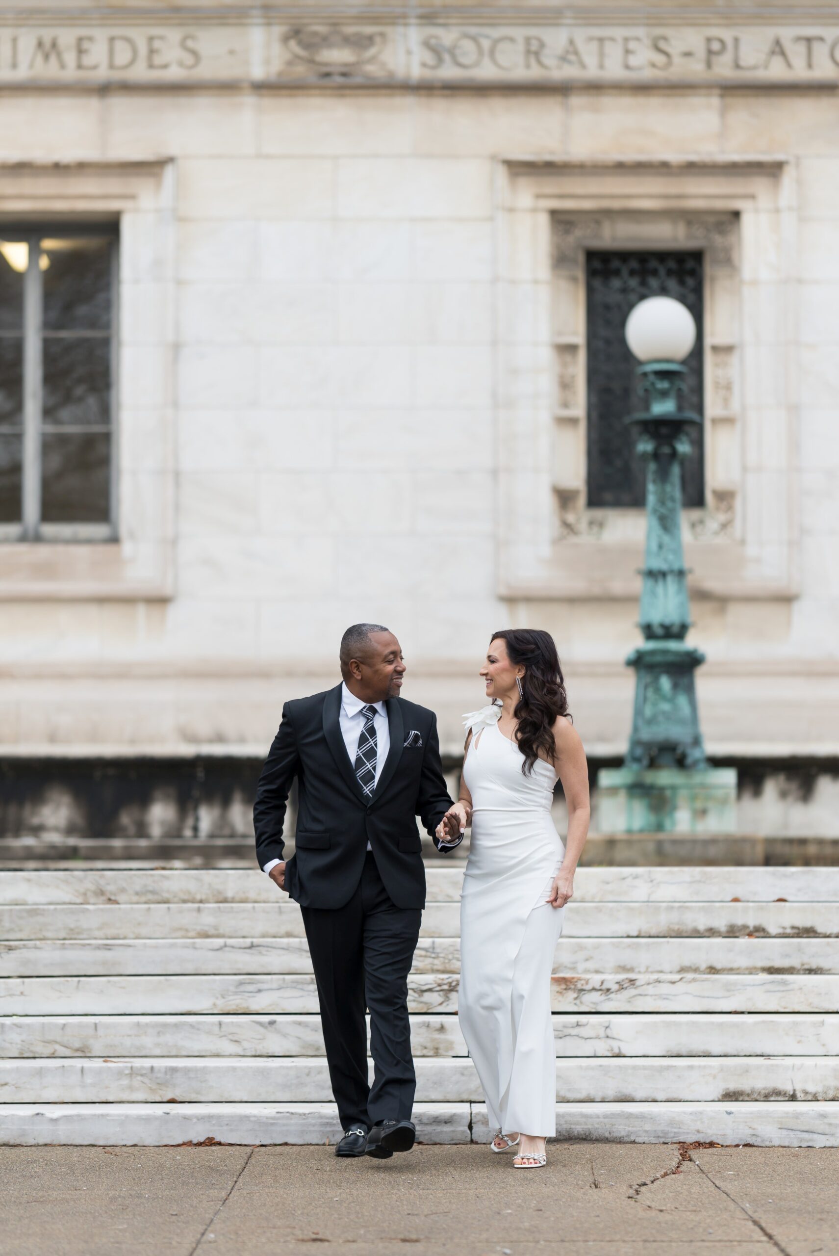 A bride and groom, holding hands, walk down the steps of the Detroit Public Library on Woodward on their wedding day.  