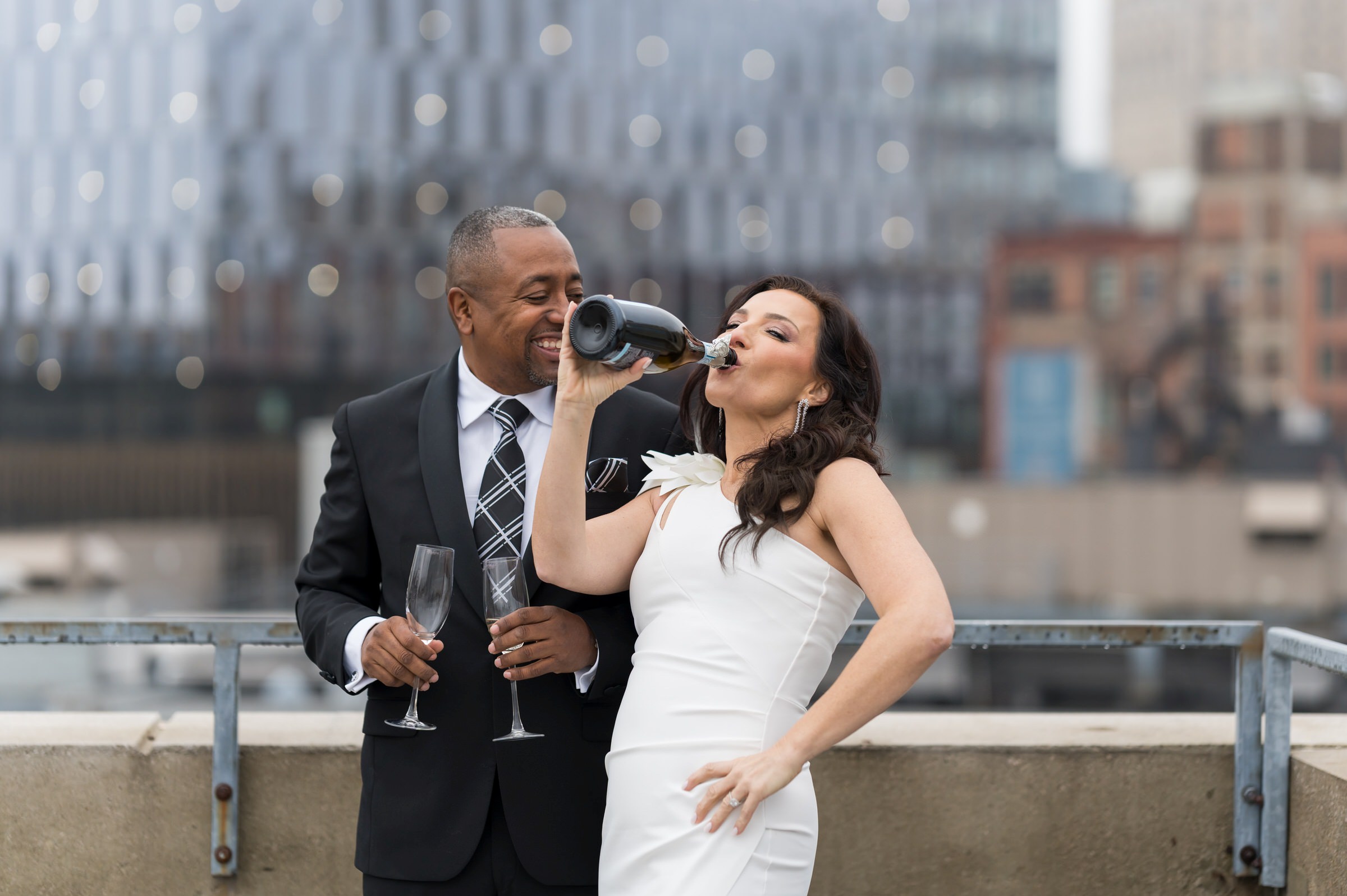 A bride chugs champagne out of the bottle on their wedding day atop of a rooftop in Detroit.  