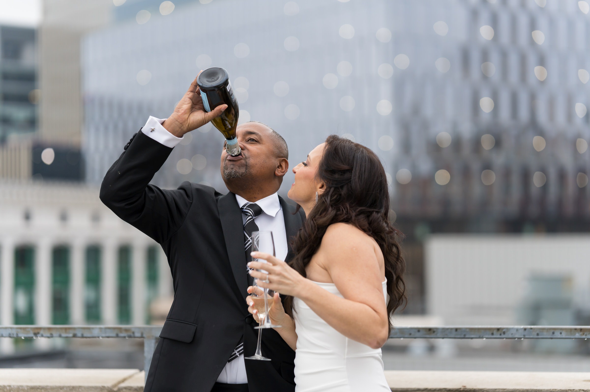 A groom chugs champagne out of the bottle on their wedding day.  