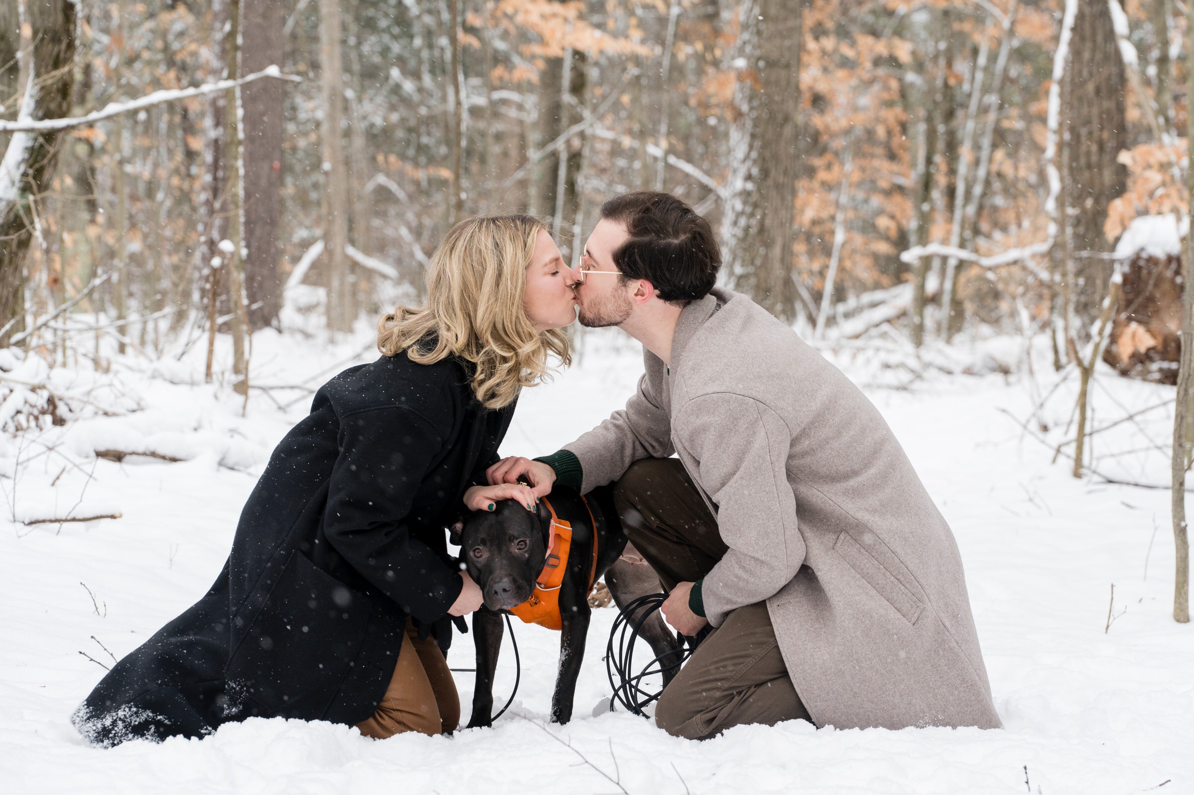 A couple, both kneeling in the snow, celebrate with a kiss after their Getaway proposal.  