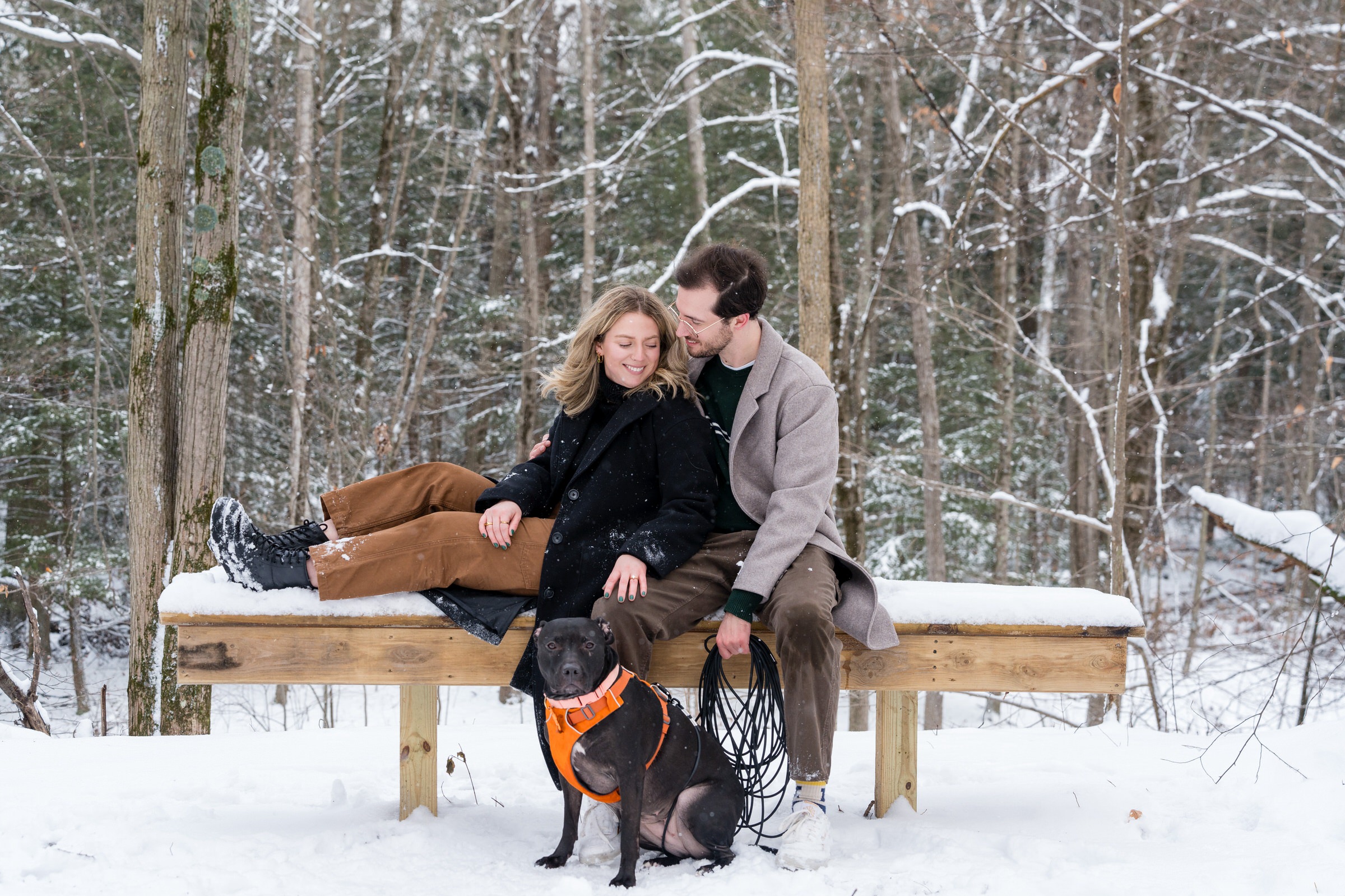 A couple sits on a snow covered bench after their Getaway proposal.