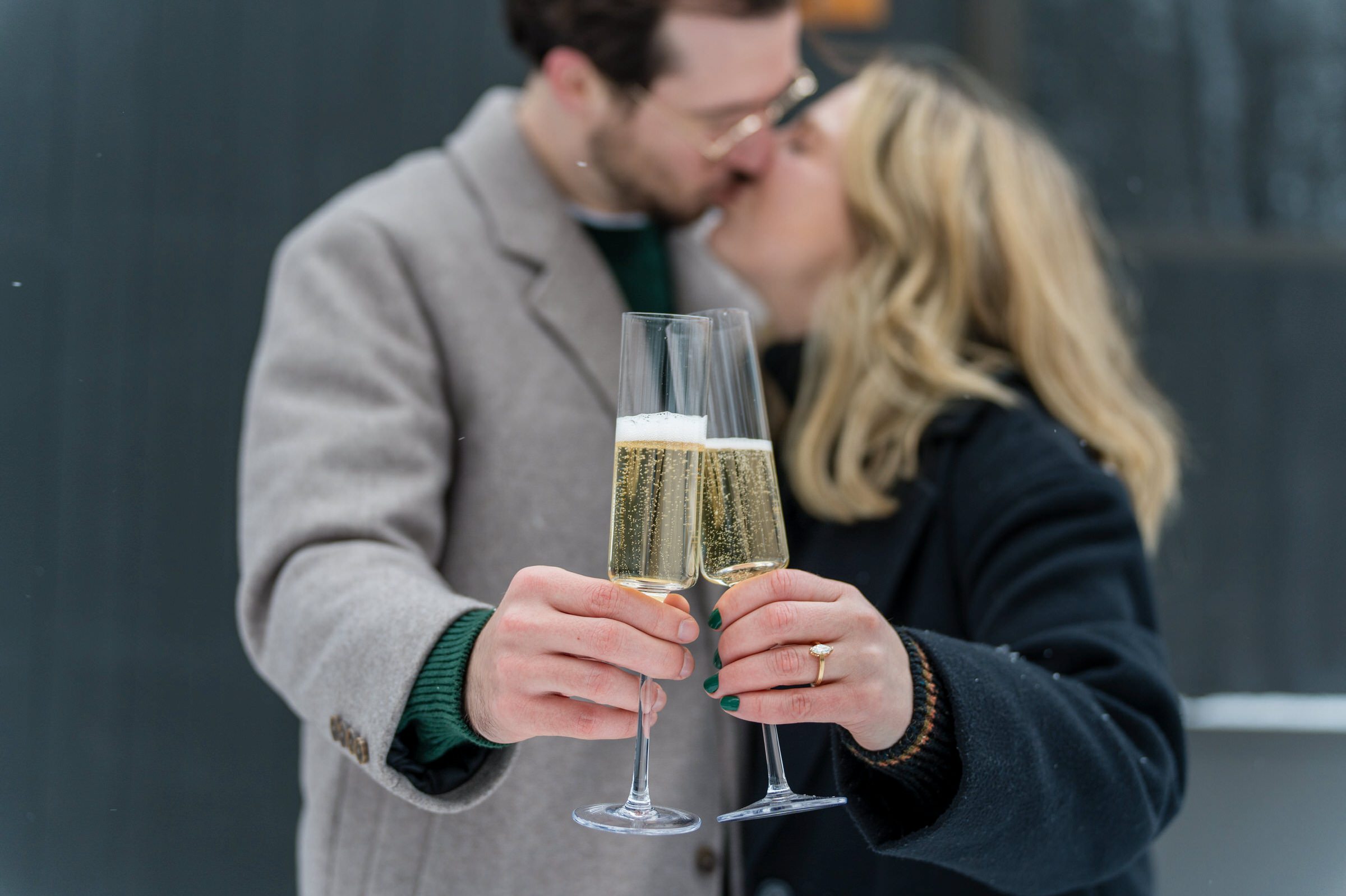 Champagne glasses clink with a kissing couple in the background.  