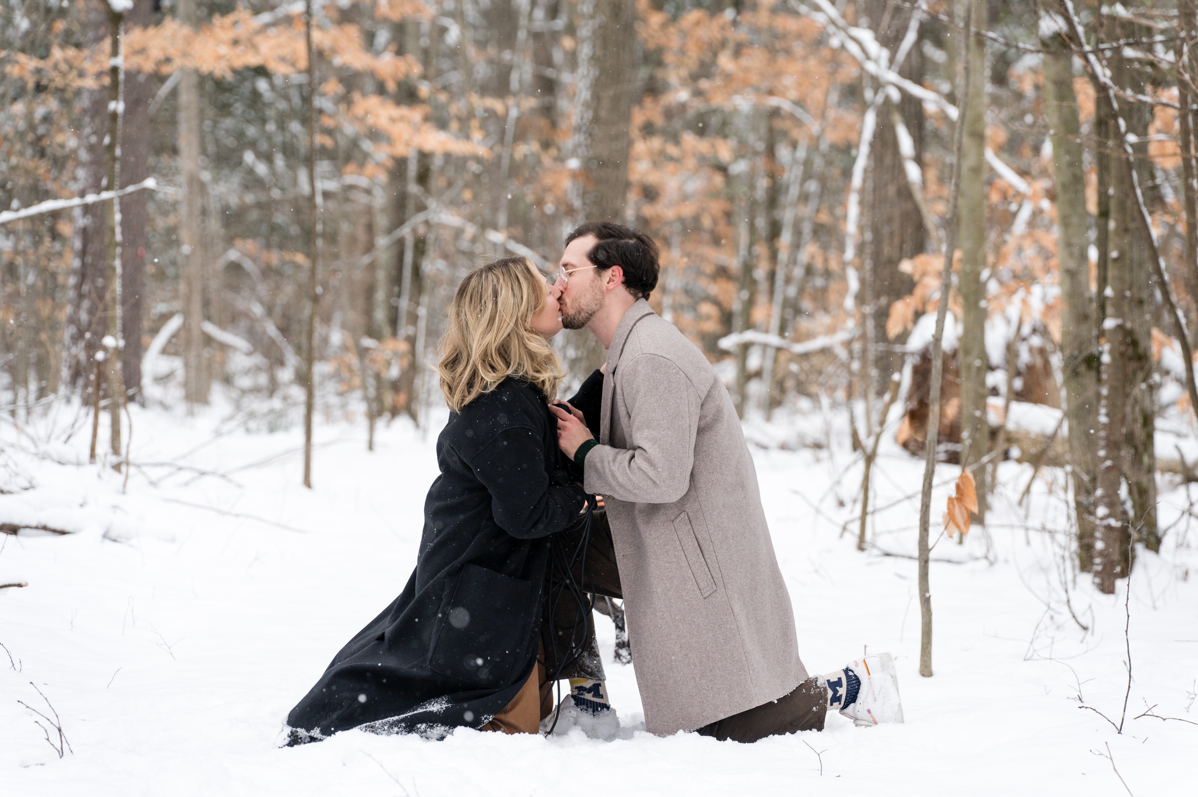 A couple, both kneeling in the snow, kiss after their Getaway proposal.  