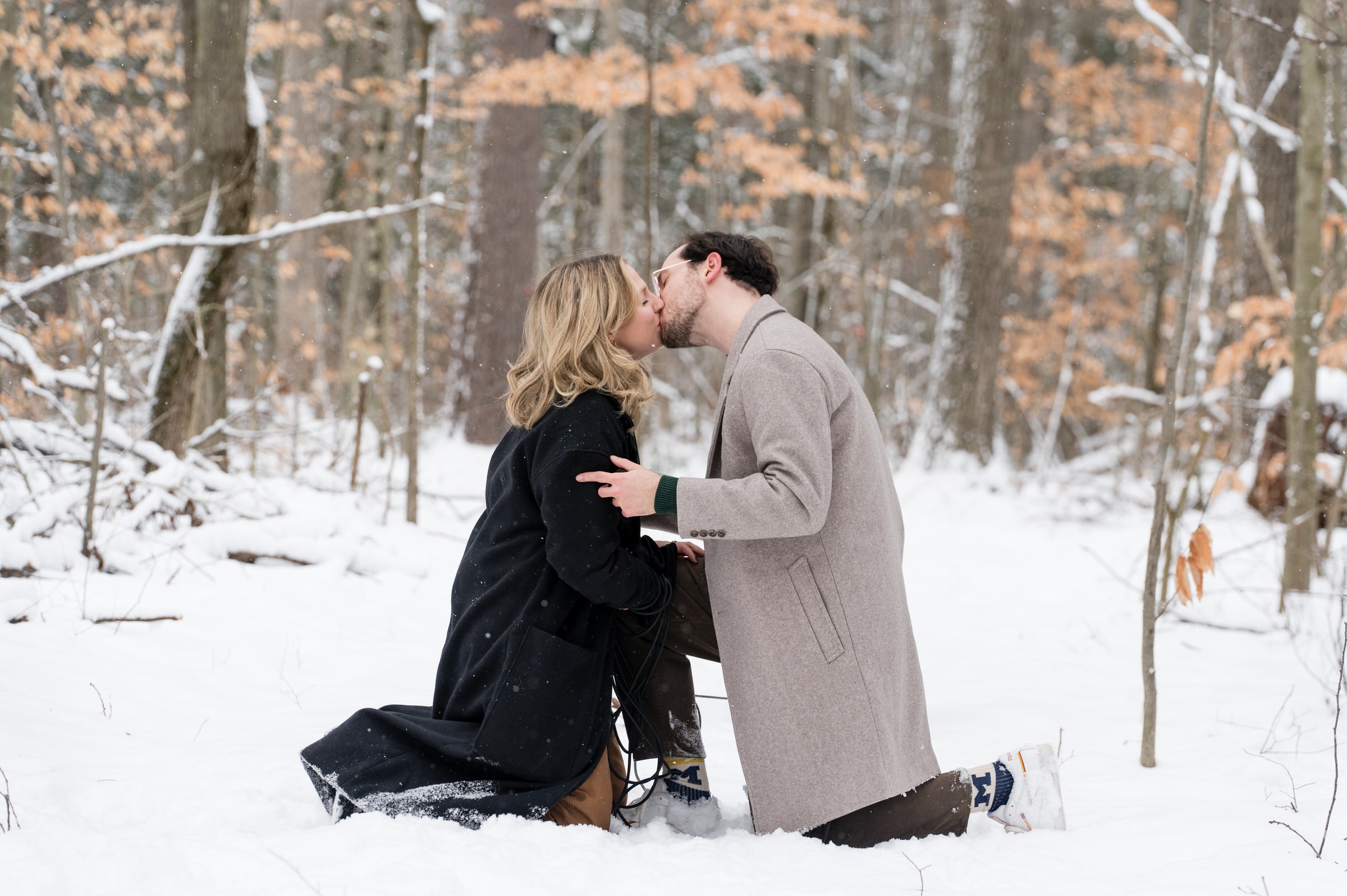 A couple, both kneeling in the snow, kiss after their Getaway proposal.  