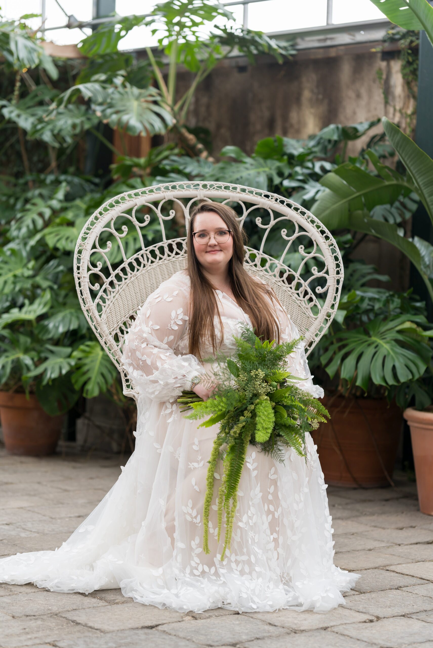 The bride sits in a white chair, holding a green bouquet, at her Planterra wedding. 