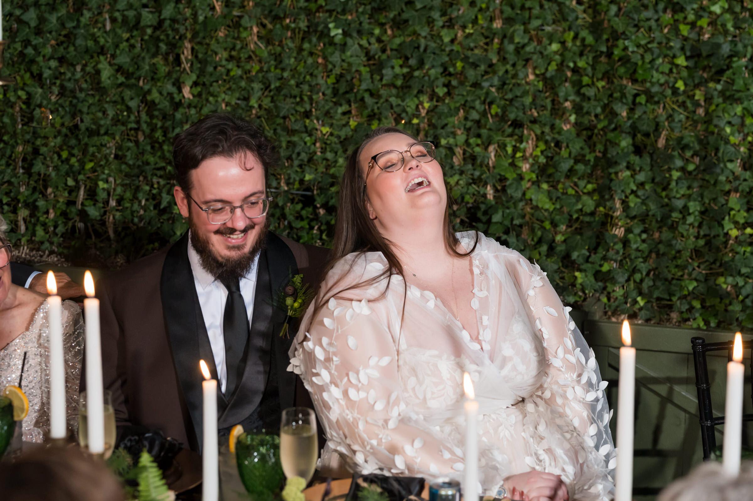 A bride and groom laugh during speeches at their Planterra wedding. 