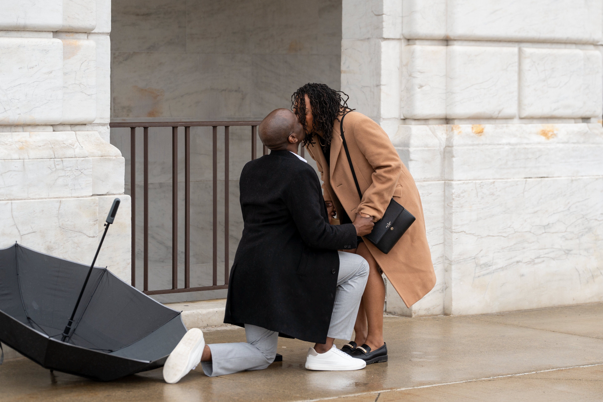 A couple kisses during a marriage proposal at the DIA in the rain.  