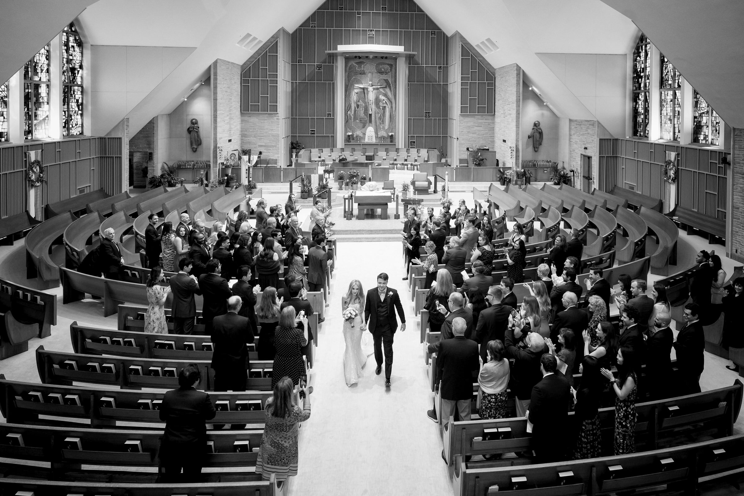 A bride and groom wave as they walk down the aisle of Holy Name Church.  