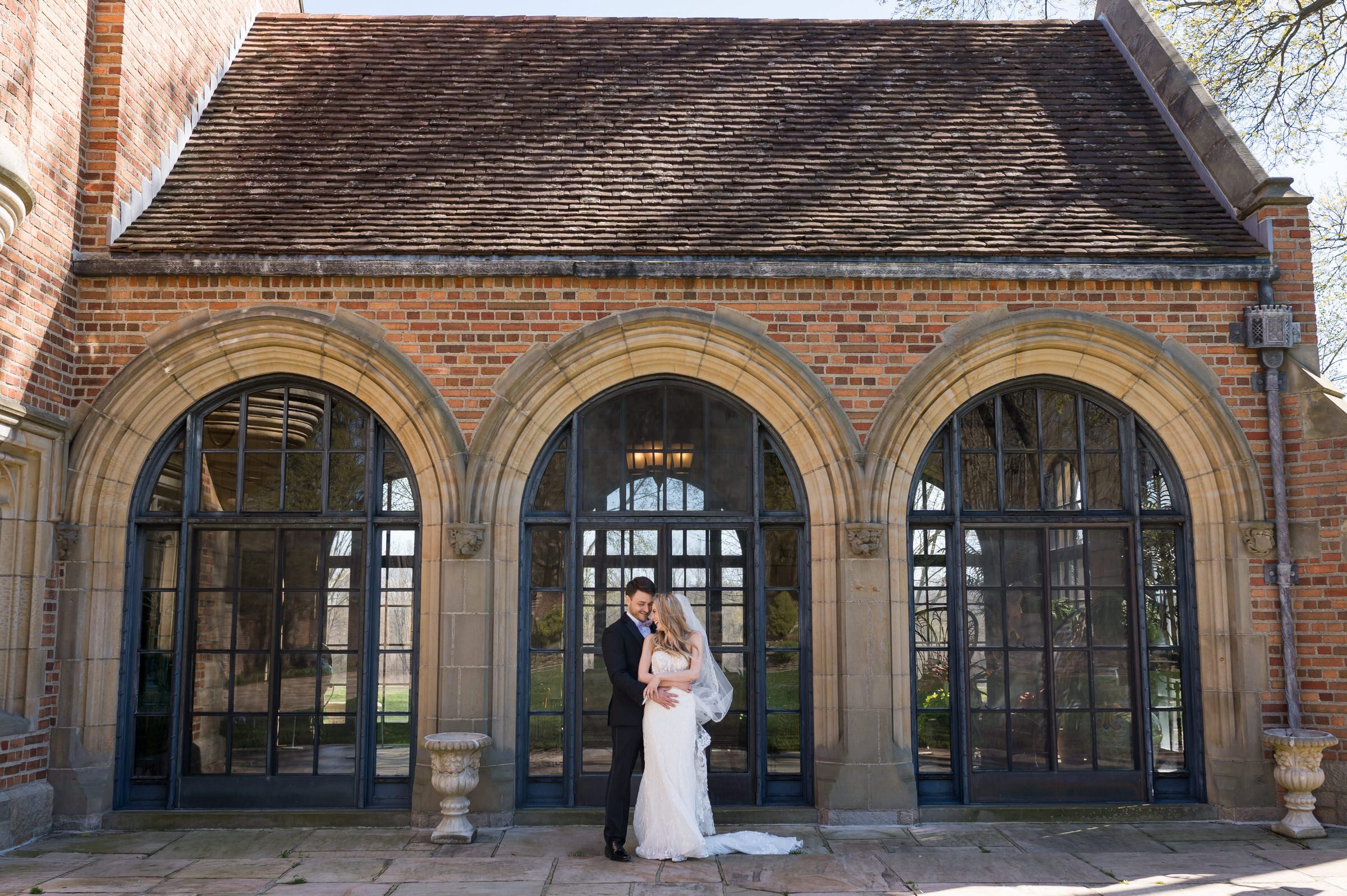 A bride and groom stand in front of windows at their Meadowbrook wedding.  