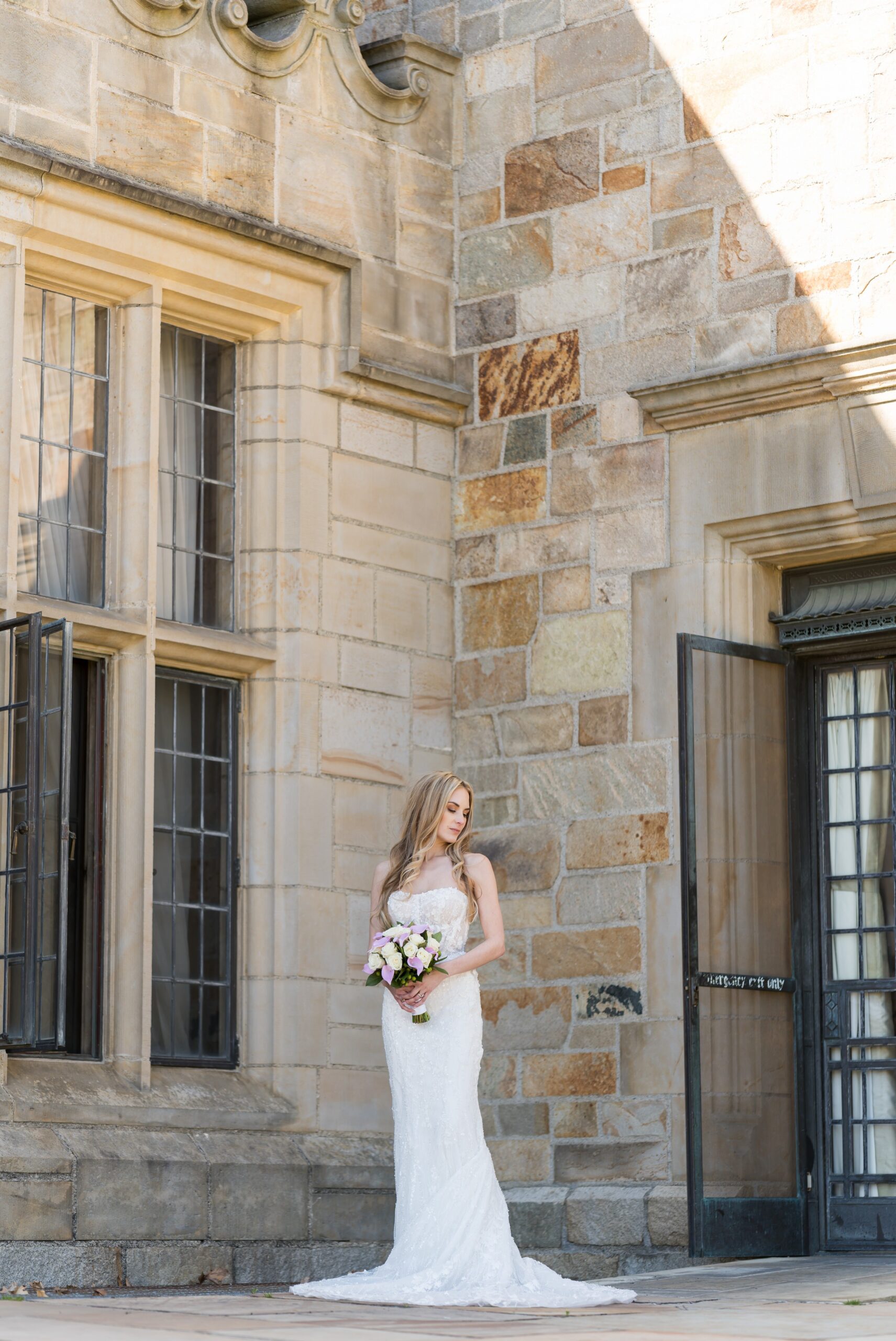 A bride stands in the corner outside of Meadowbrook Hall on her wedding day.  