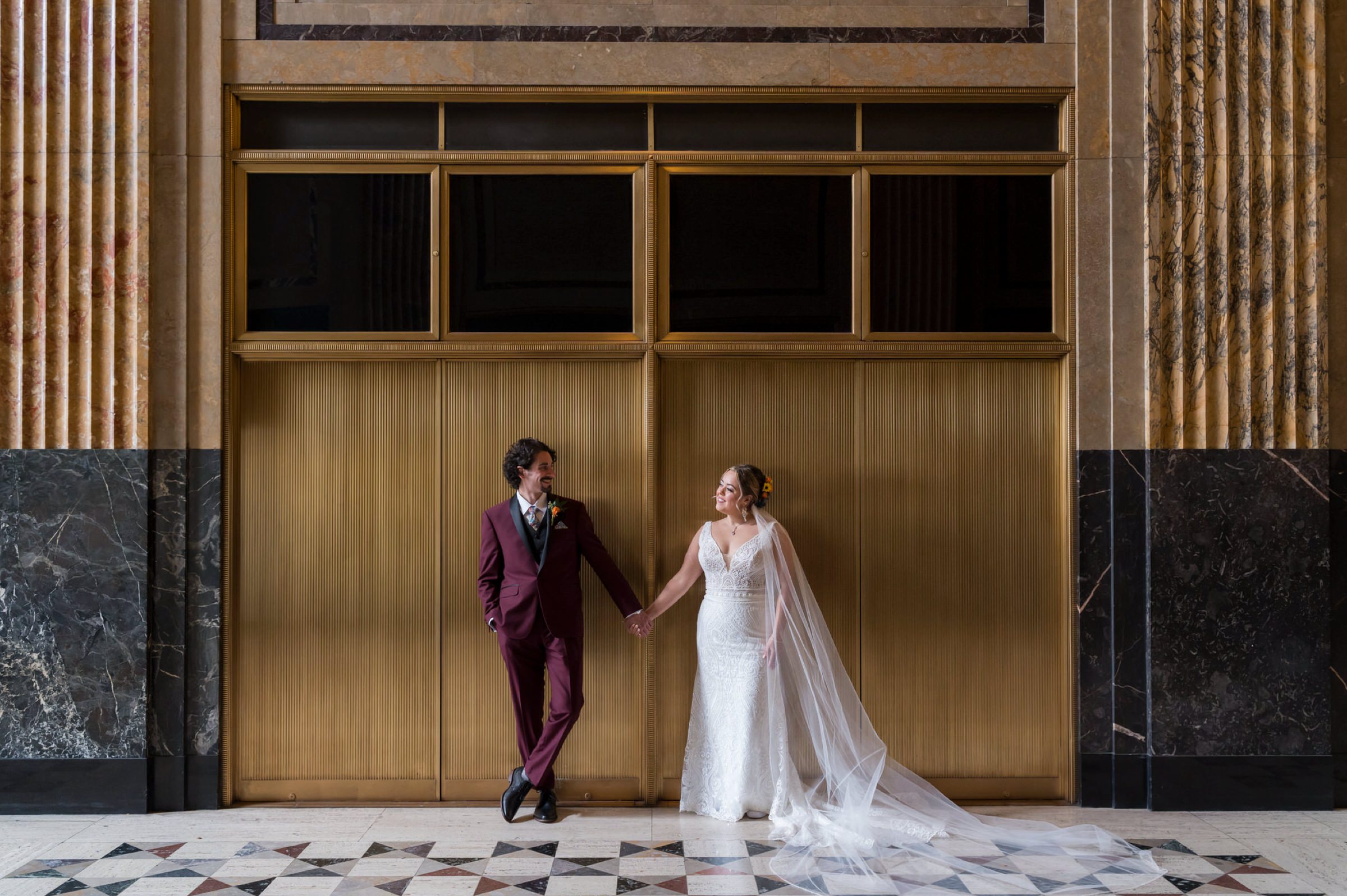 A bride and groom hold hands and look at each other at the Fisher Building on their wedding day.  