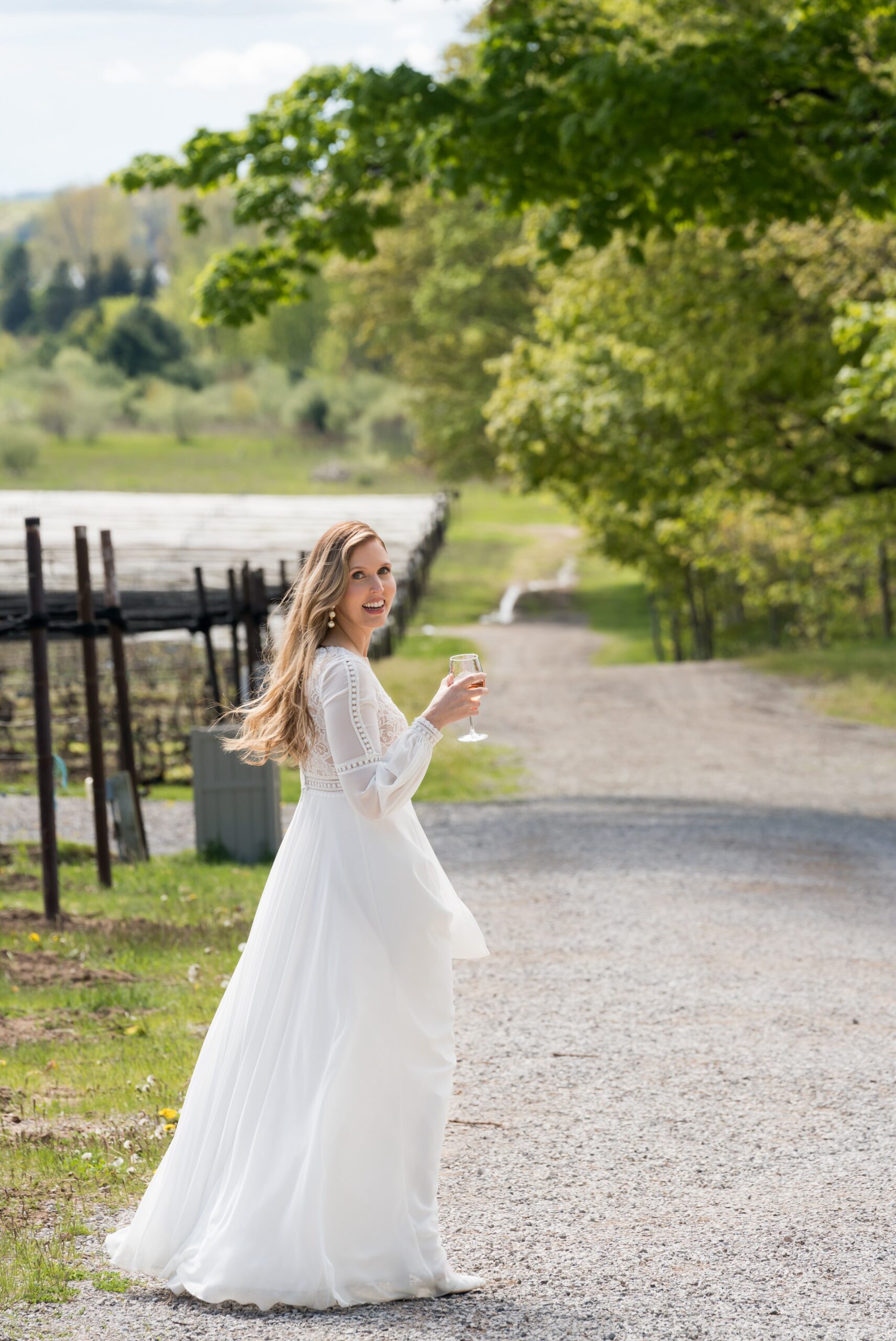 A bride walks the vineyard with wine glass in hand during Traverse City wedding.  
