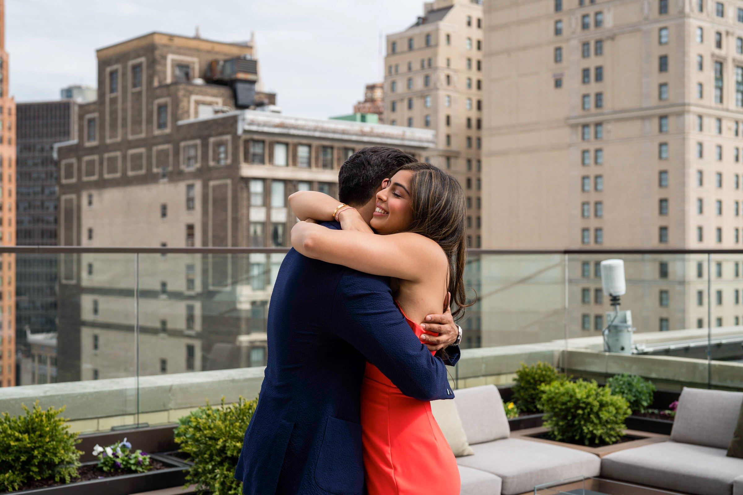 A couple hugs and reacts to her Kamper's Rooftop Proposal atop the Book Tower in Detroit.  